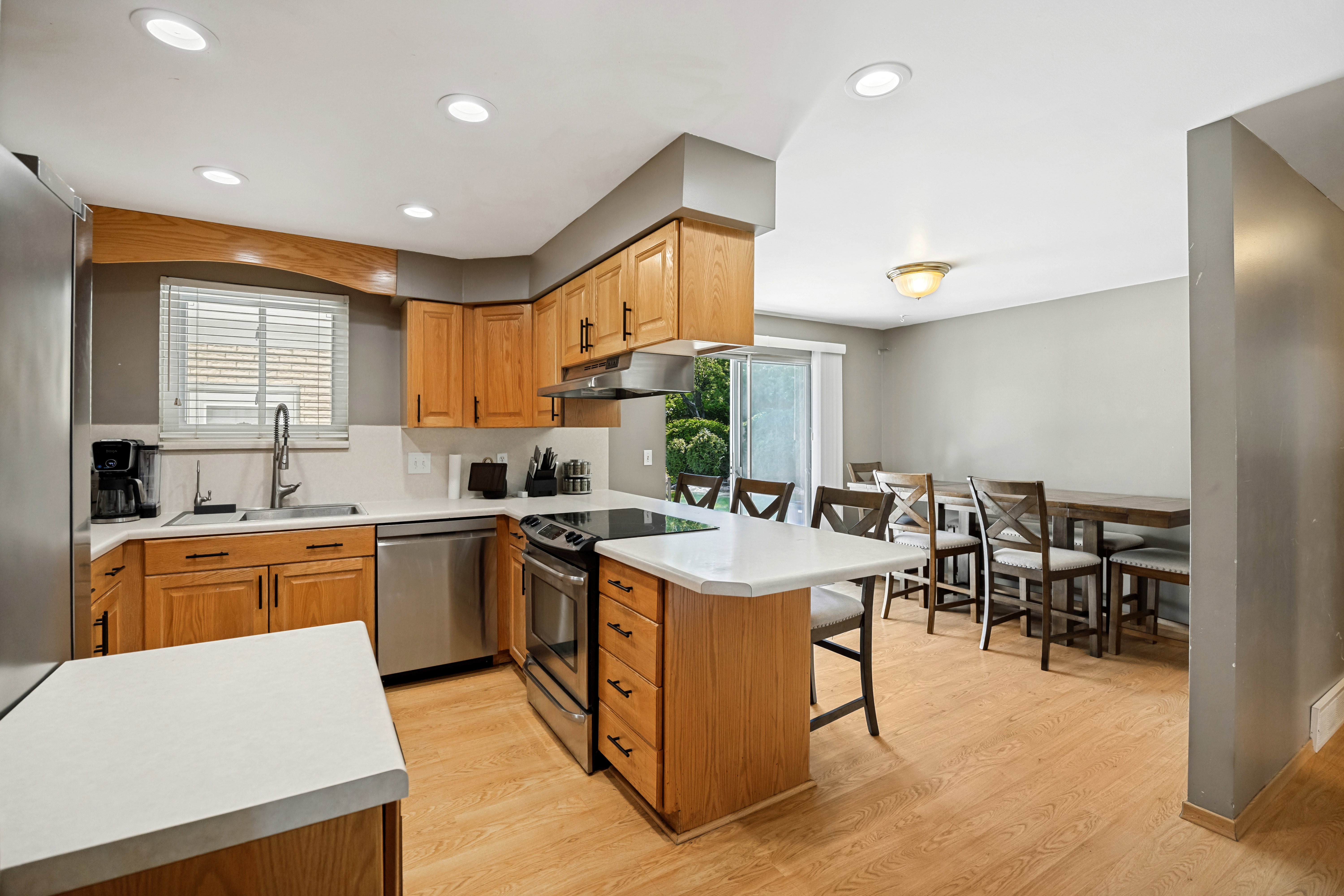Kitchen and dining area featuring wood-finish flooring, light wood cabinetry, white countertops, and stainless steel appliances