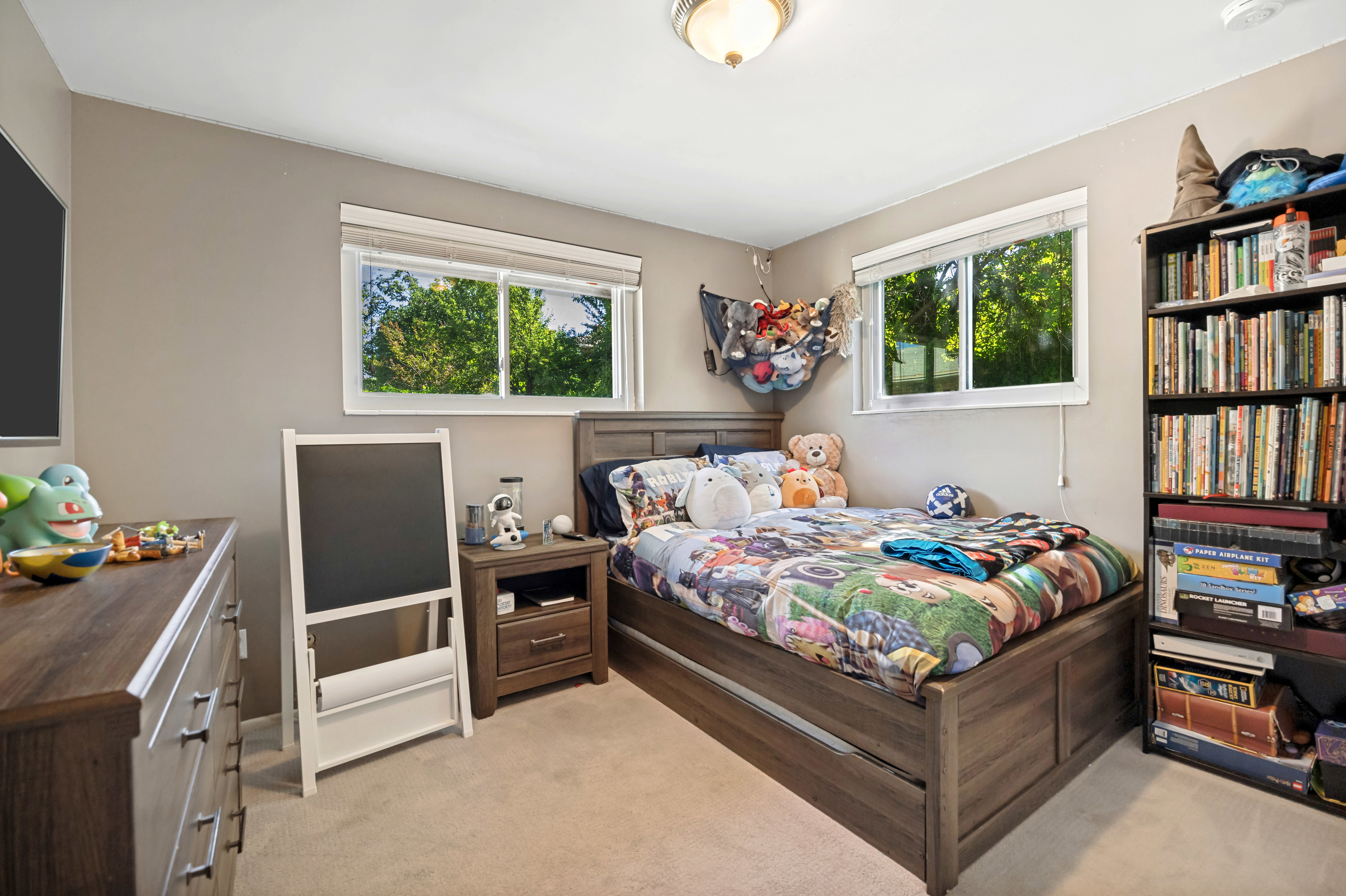 Carpeted bedroom featuring two windows with white trim, a wood-finish bed frame, and a built-in ceiling light fixture