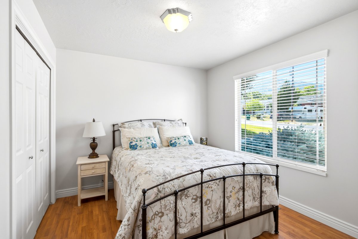 Bedroom featuring wood-finish flooring, a large window with blinds, and a bi-fold closet