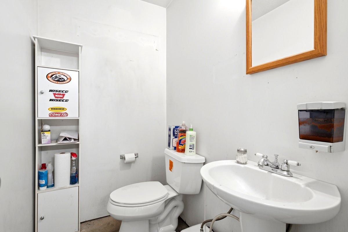 Pedestal sink with chrome faucet, toilet, and wall-mounted mirror with a wood frame