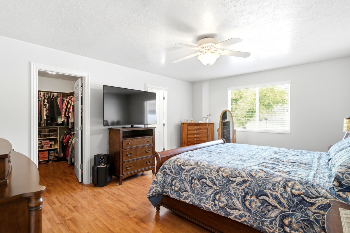 Room with wood-finish flooring, a ceiling fan with integrated lighting, a window with horizontal blinds, and a walk-in closet with built-in shelving