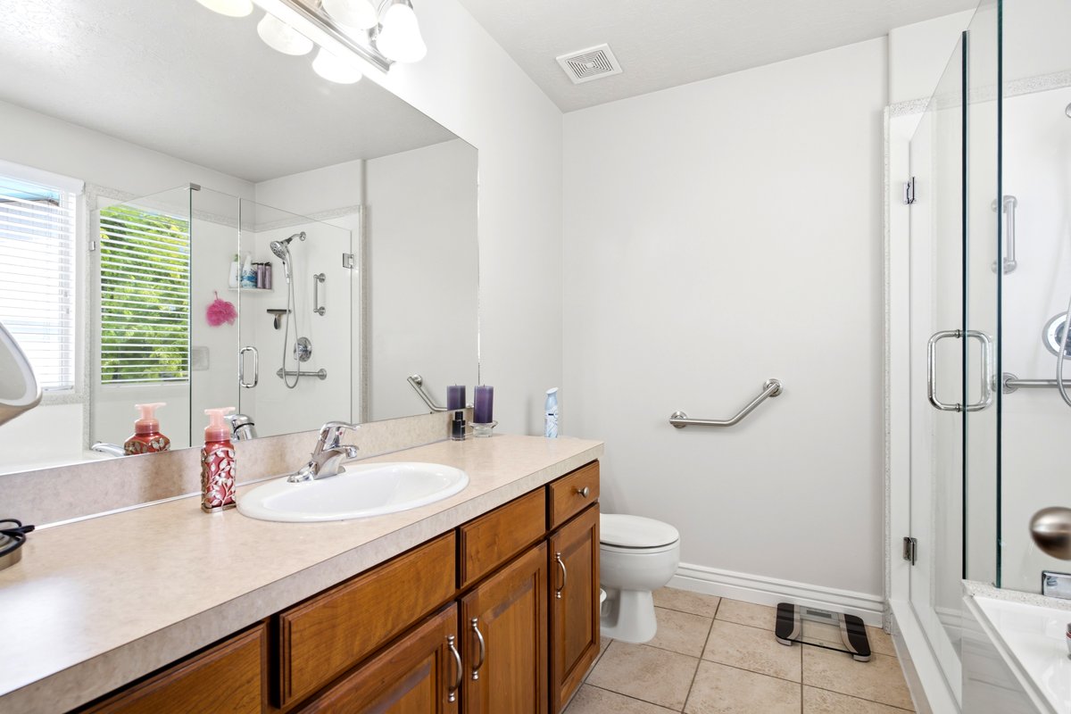 Bathroom featuring a wood-finish vanity with an integrated sink, a large mirror, and a glass-enclosed shower with grab bars