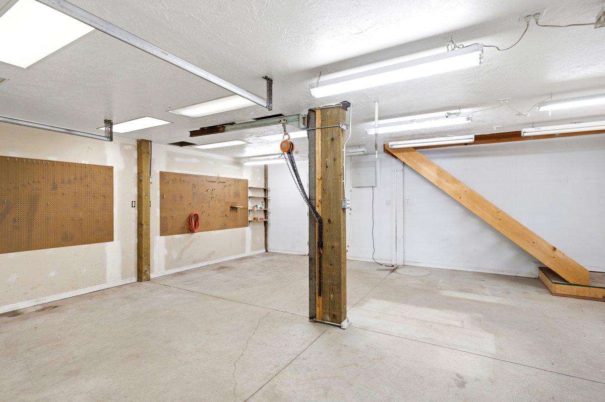 Spacious utility area featuring a concrete floor, multiple fluorescent light fixtures, overhead track system, and wall-mounted shelving