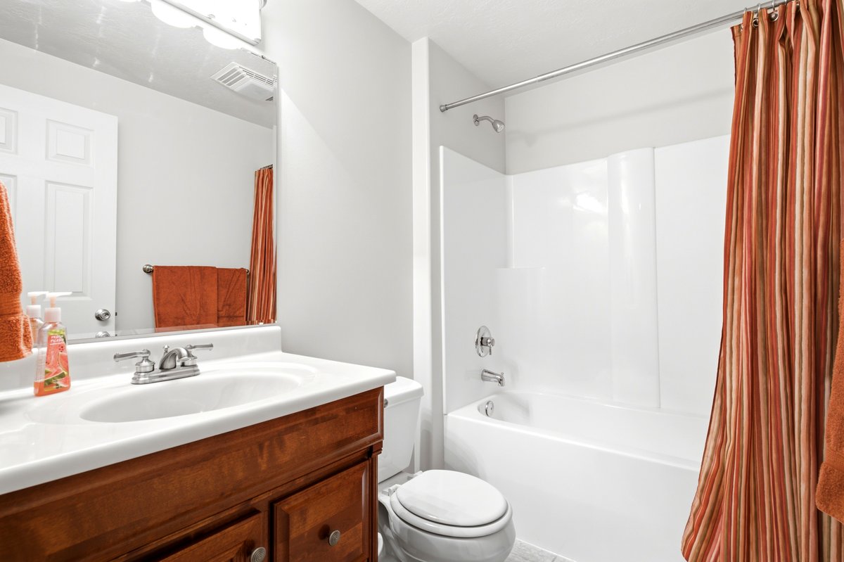 Bathroom featuring a wood-finish vanity with a white countertop and integrated sink, chrome faucet, wall-mounted mirror, and a white tub/shower combination with a surround
