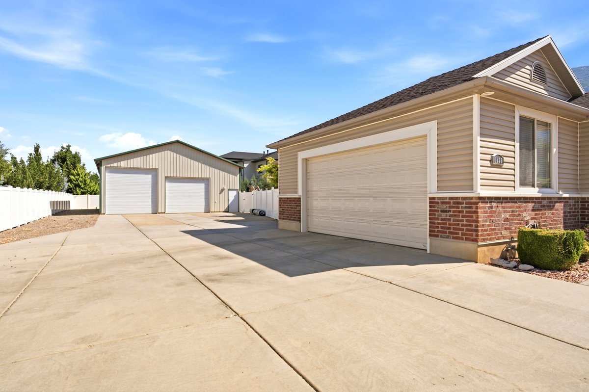 Expansive concrete driveway leading to a two-car attached garage and a separate two-bay detached outbuilding