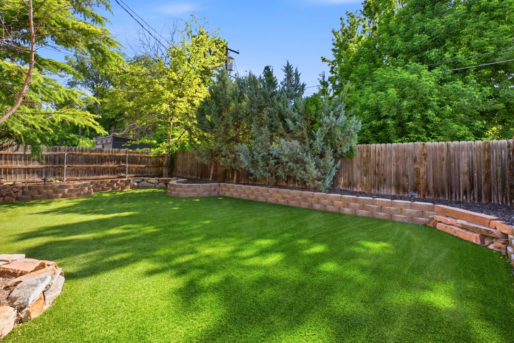 Expansive backyard featuring artificial turf, mature trees, and a wooden privacy fence