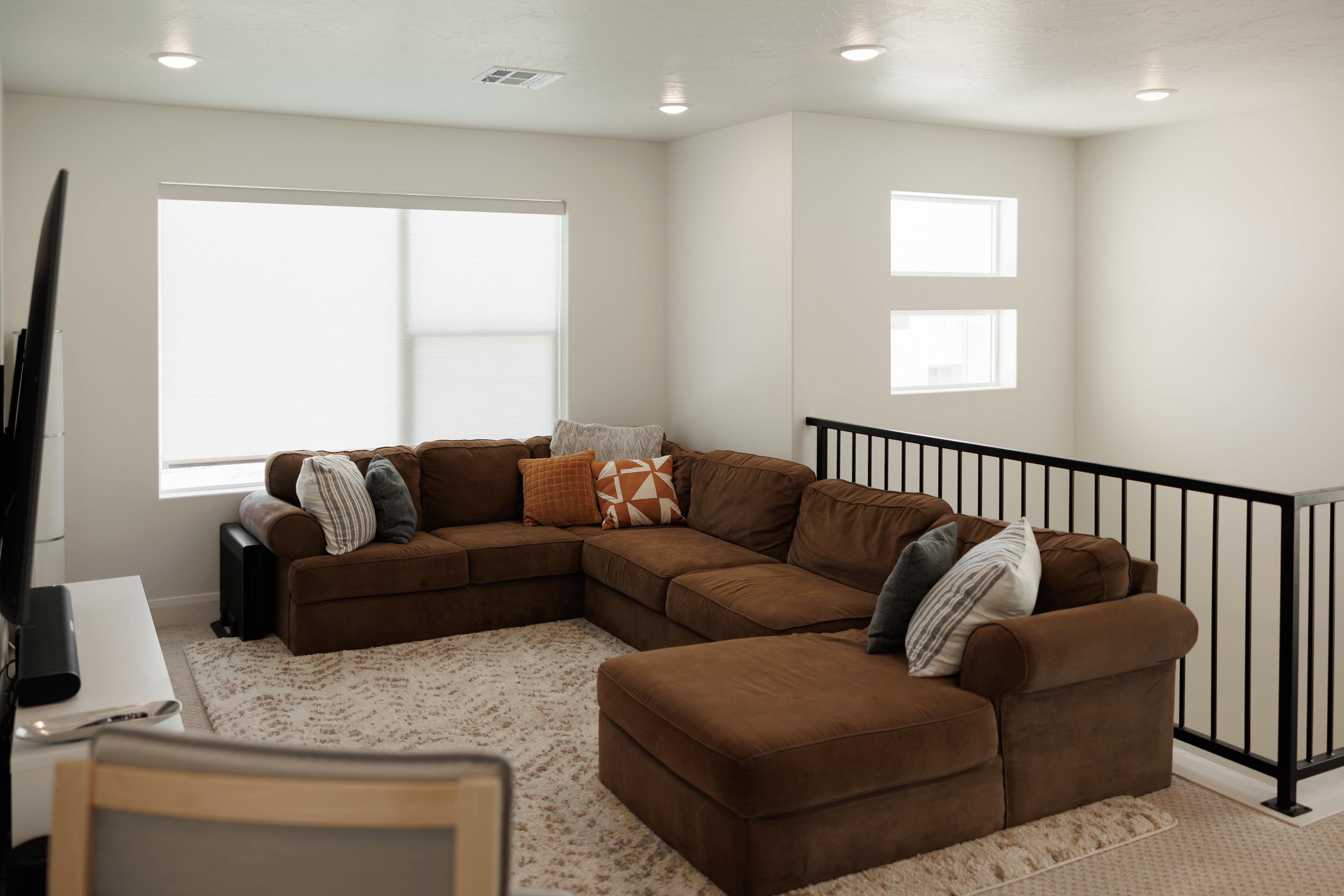 Spacious loft area featuring recessed lighting, a large window with roller shades, and a black iron railing