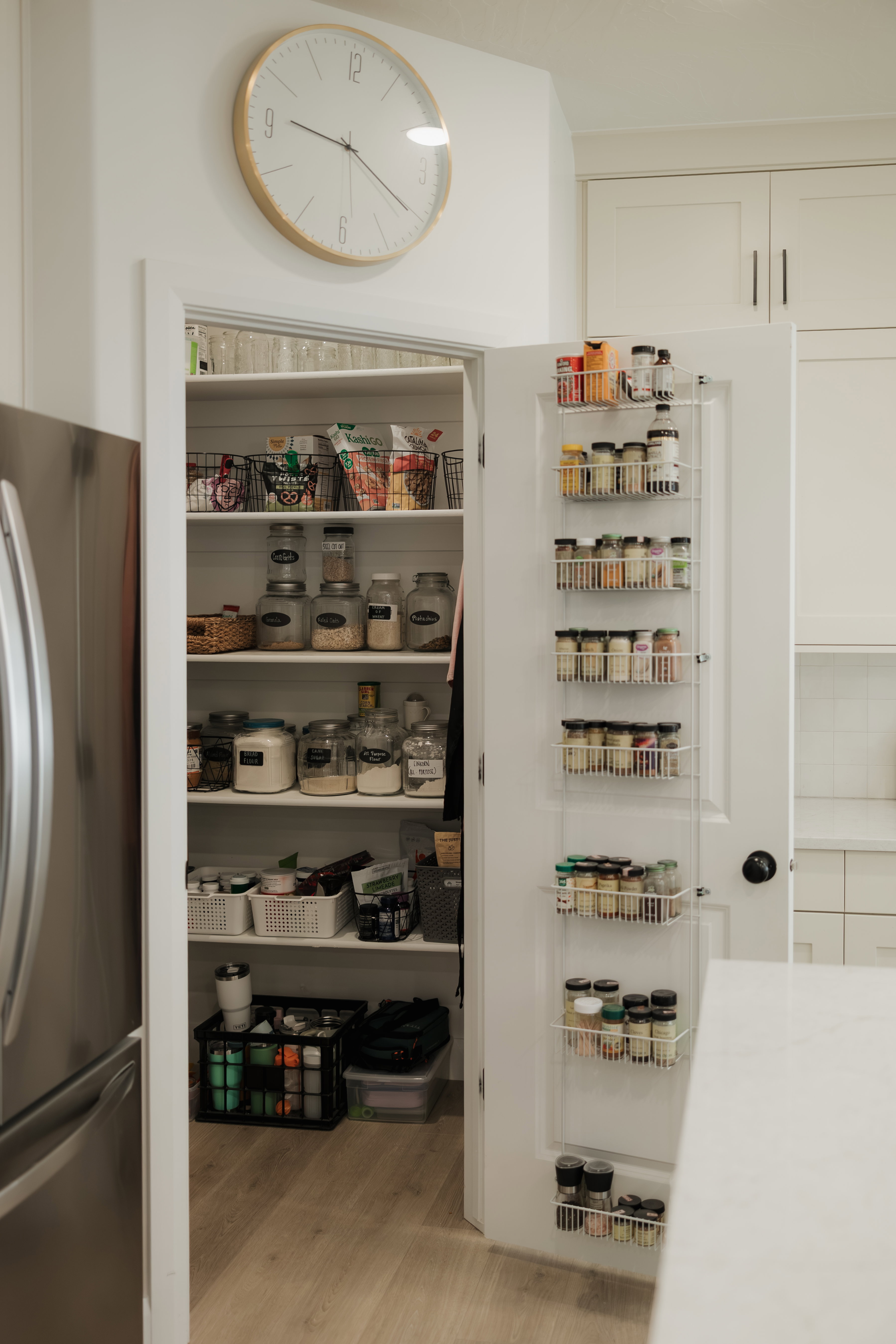 Walk-in pantry with multiple shelving units, door-mounted spice racks, and wood-finish flooring