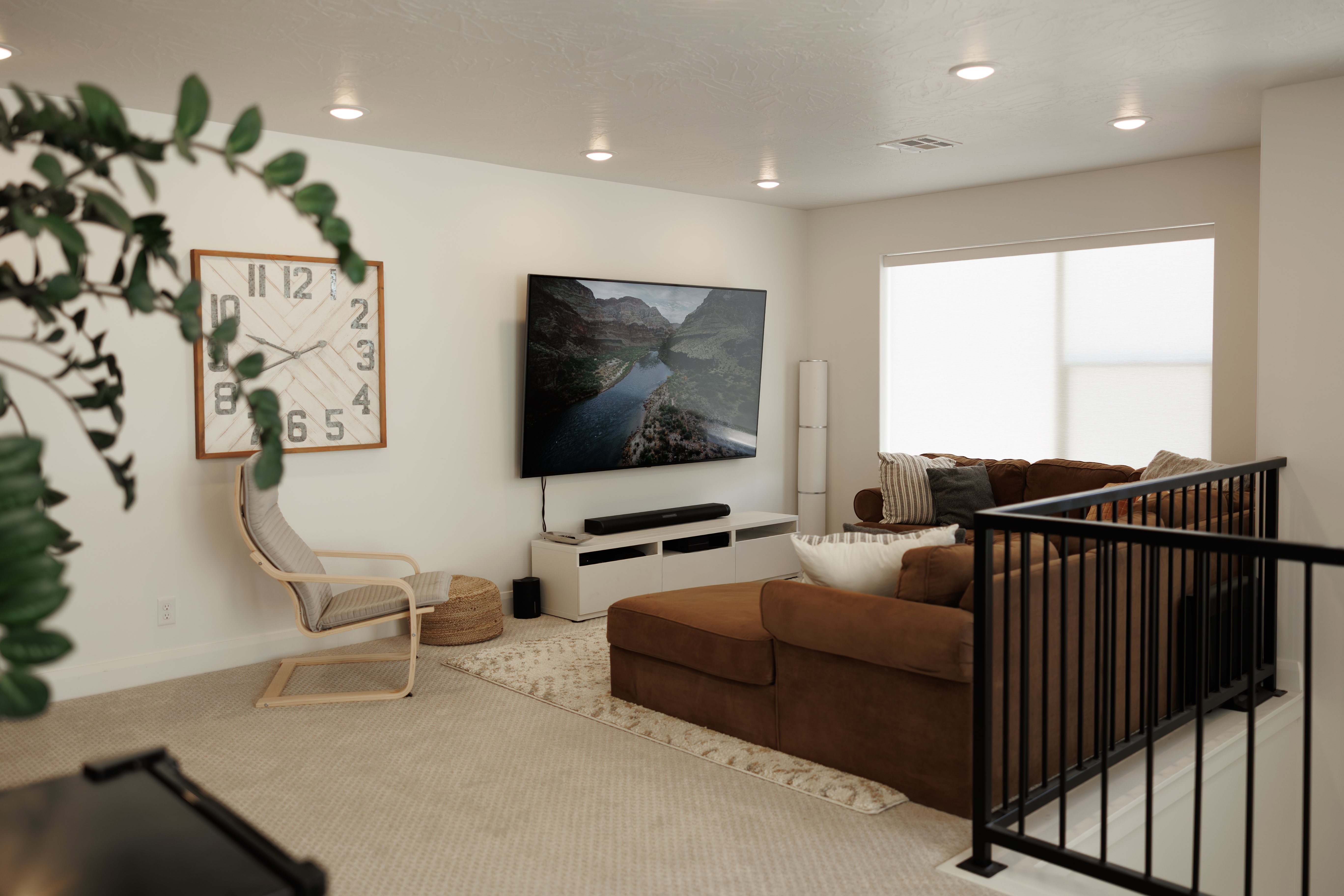 Open-concept living space with recessed lighting, large windows featuring roller shades, and a black metal staircase railing