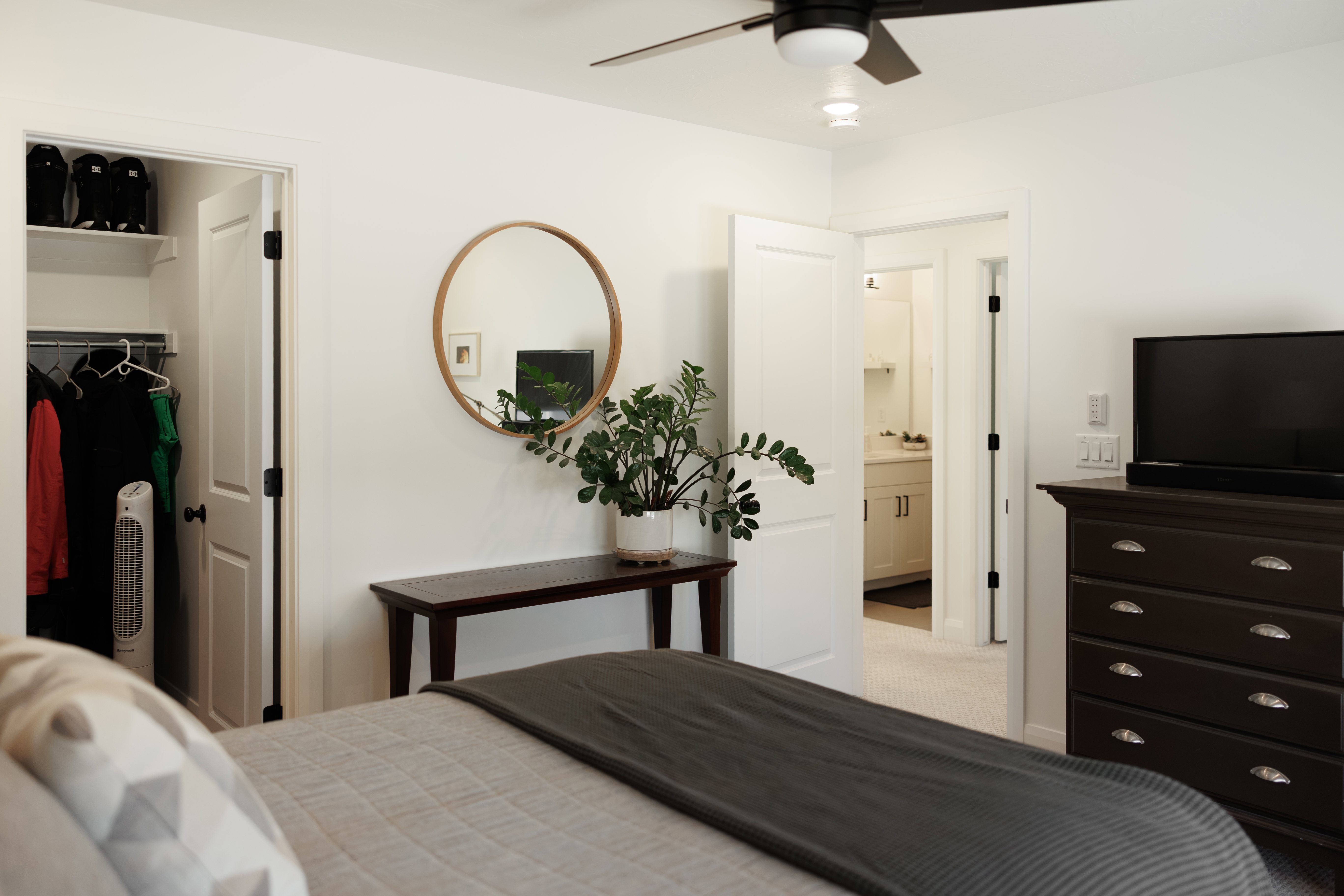 Bedroom featuring a ceiling fan with integrated lighting, a closet with shelving and hanging space, and an en-suite bathroom entry with vanity visible