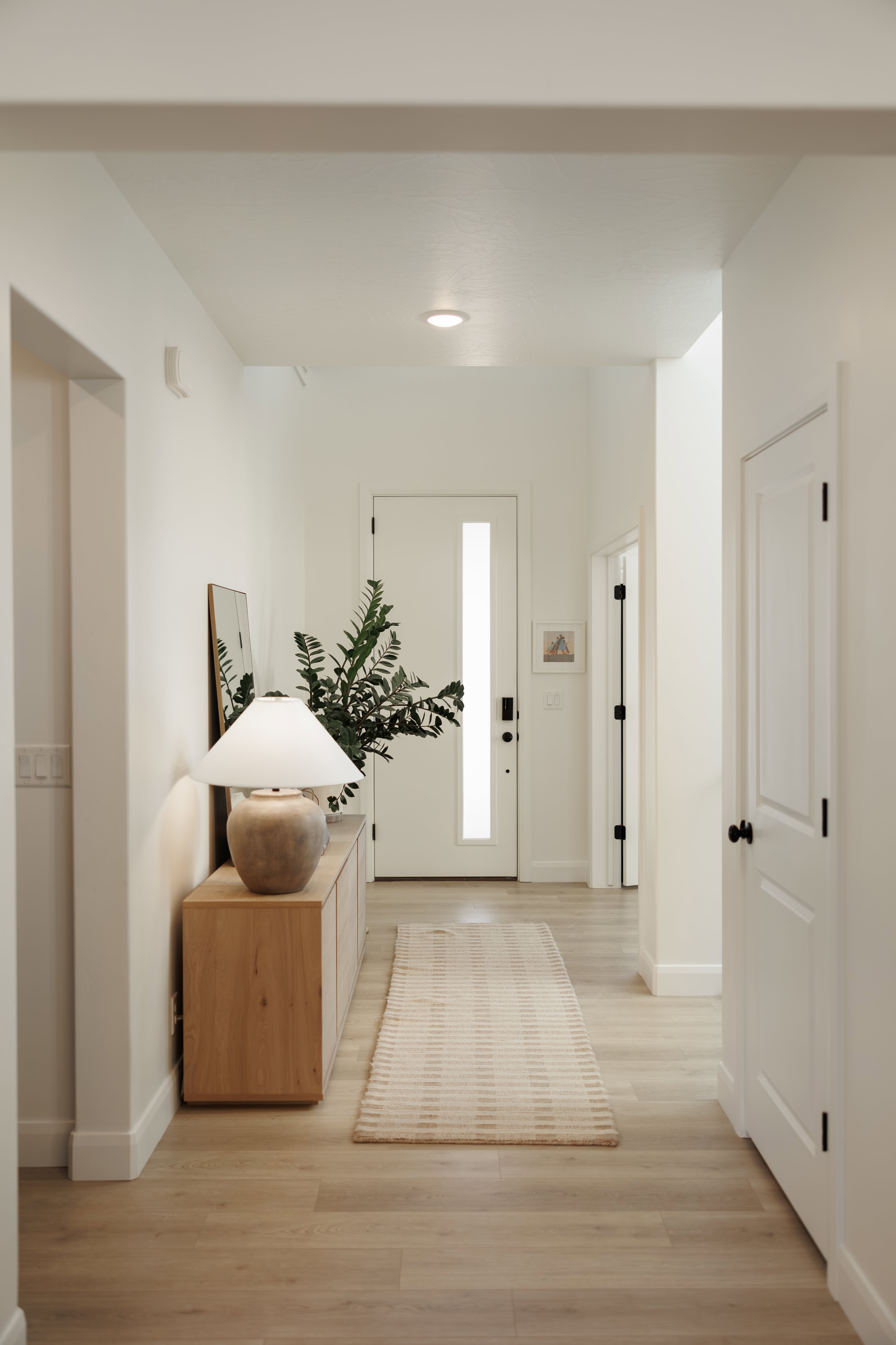 Bright hallway featuring light wood-finish flooring, recessed lighting, and a white entry door with a vertical frosted glass insert