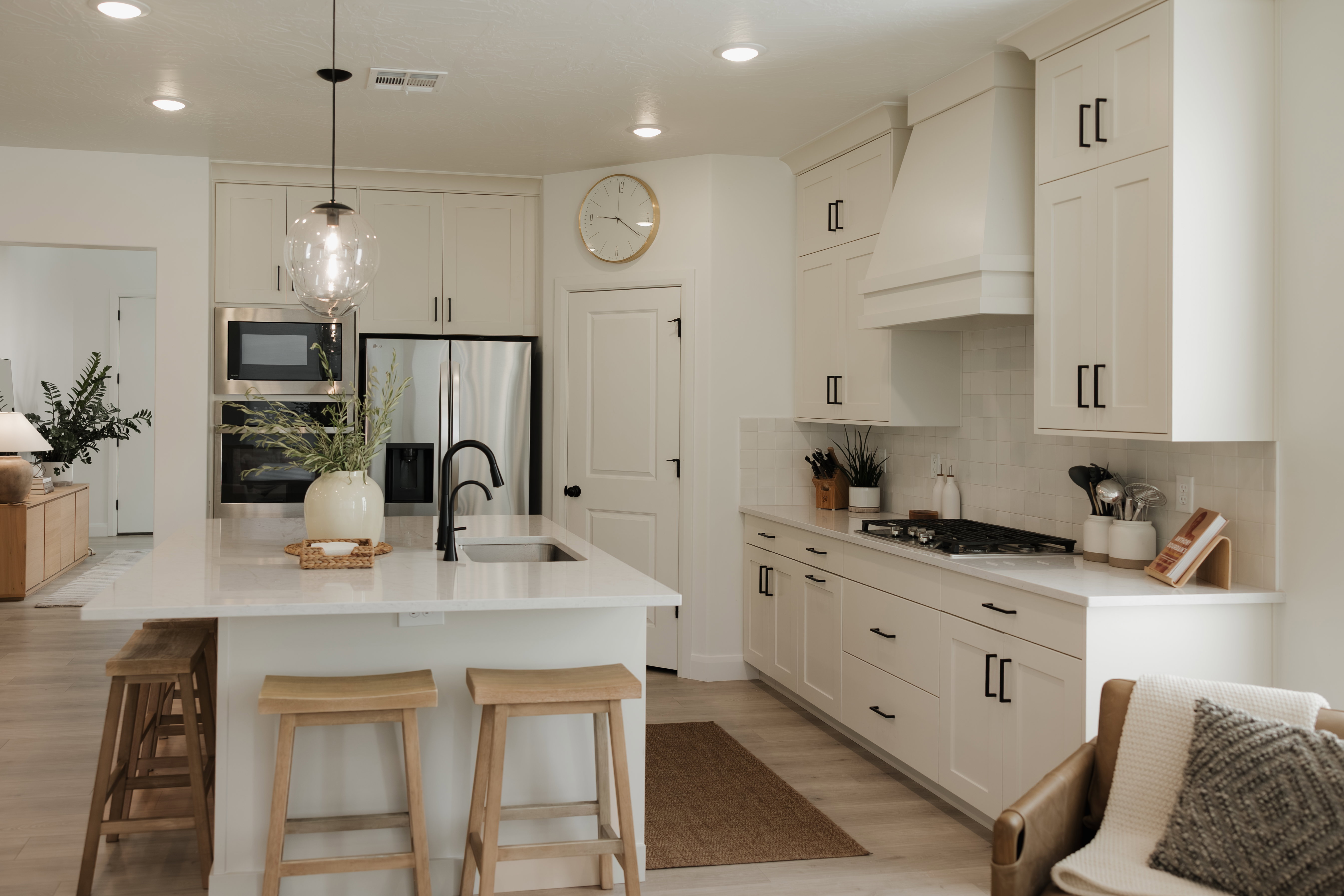 Contemporary kitchen featuring a large central island with an undermount sink, stainless steel appliances, white subway tile backsplash, and light-toned cabinetry with matte black hardware
