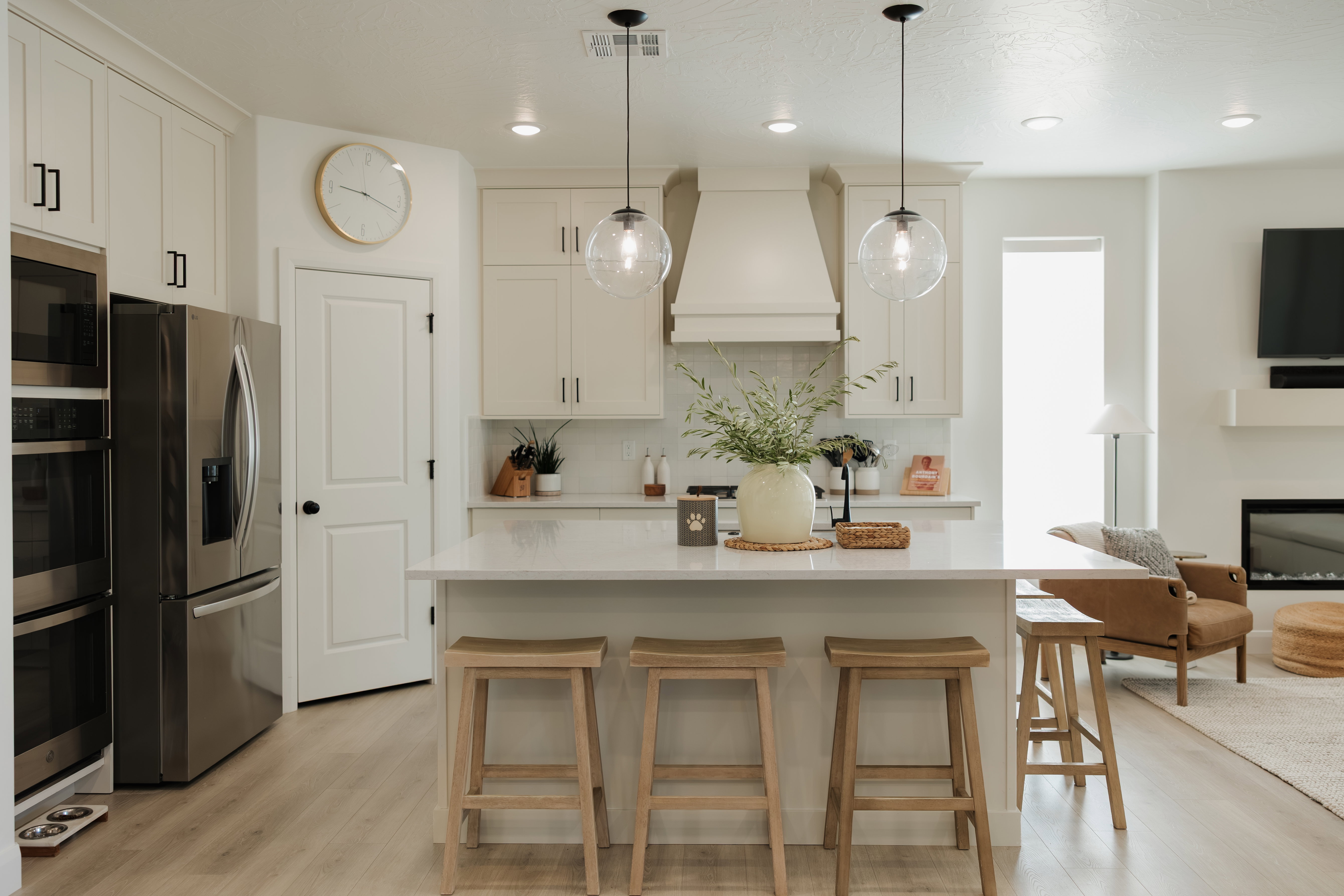 Open-concept kitchen featuring an island with seating, stainless steel appliances, light-toned cabinetry, a built-in range hood, and wood-finish flooring