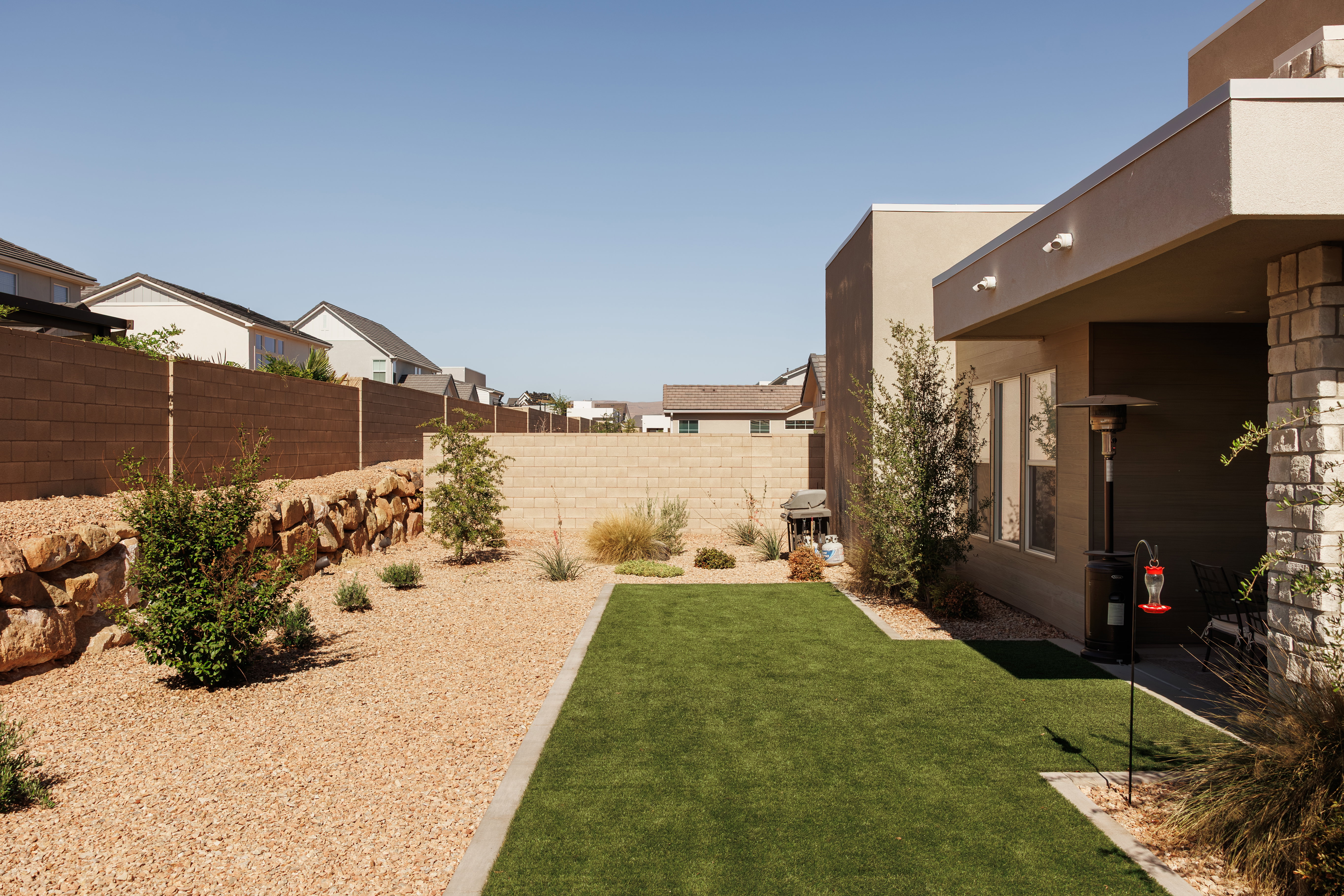 Backyard featuring a synthetic lawn, gravel landscaping, and a rock retaining wall