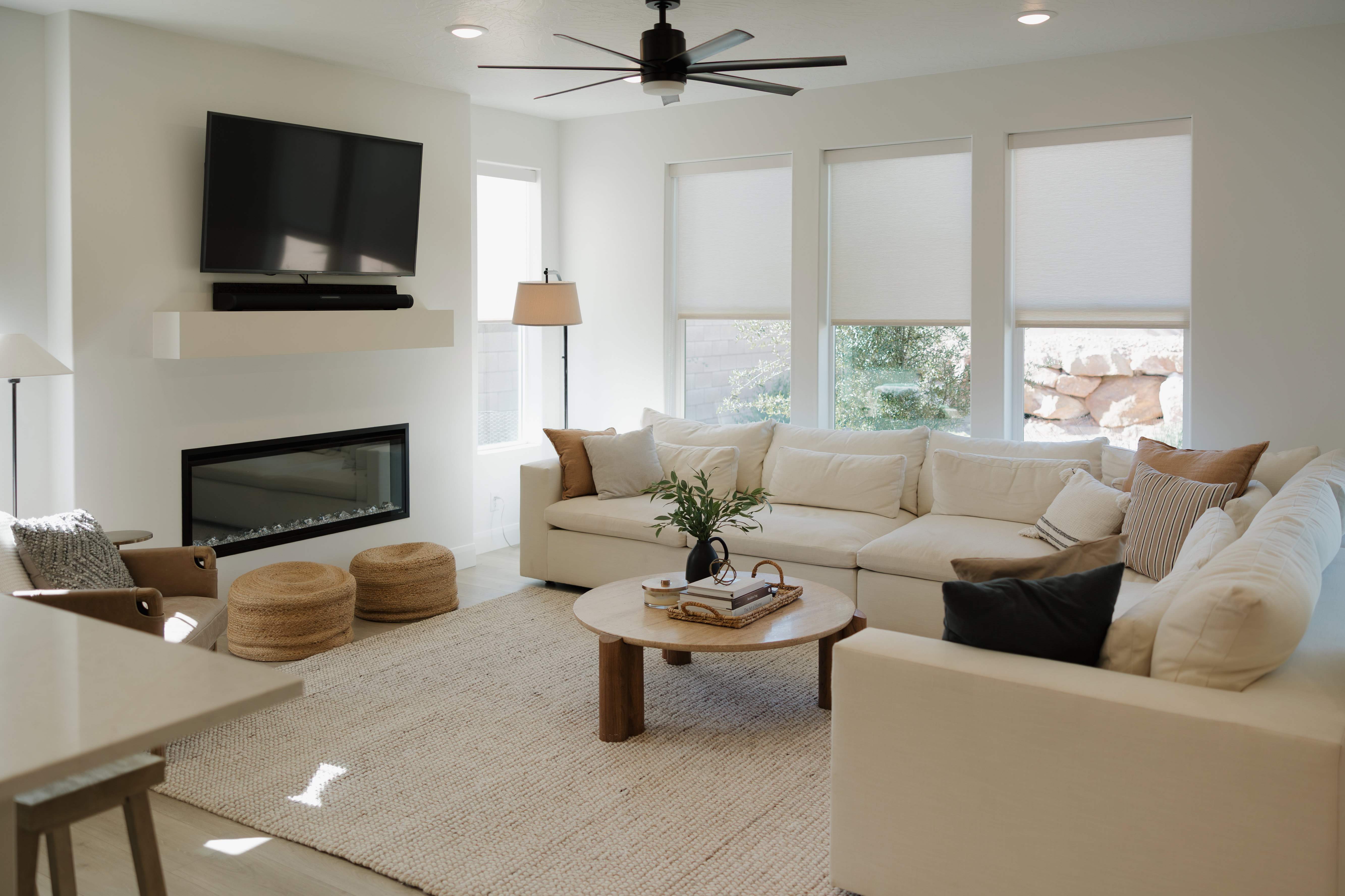 Living area featuring a modern fireplace with a floating mantel, large windows with roller blinds, a ceiling fan with integrated lighting, and light wood-finish flooring
