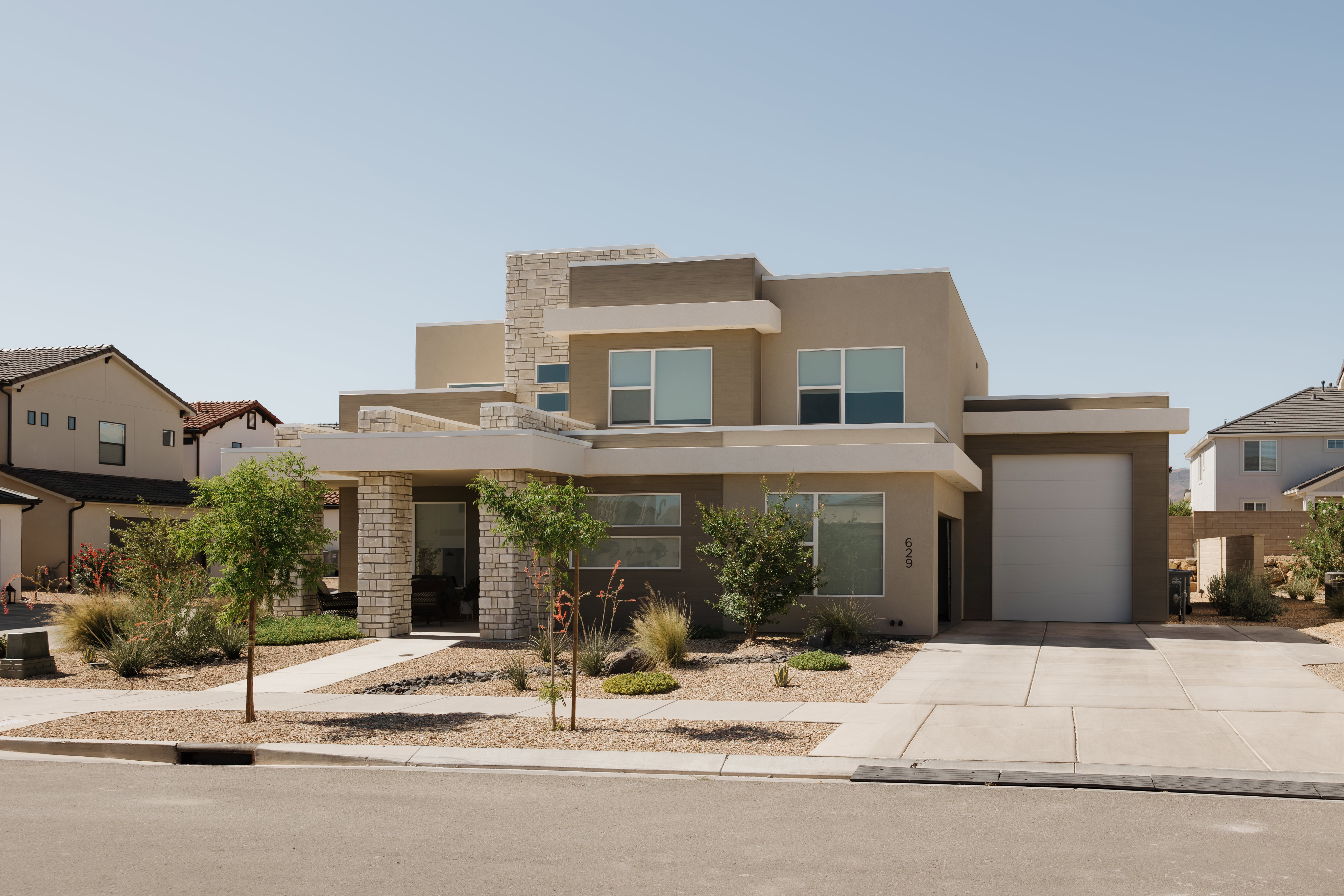 Modern stucco exterior with stone accents, a concrete driveway, a front walkway, an integrated garage, and low-maintenance landscaping