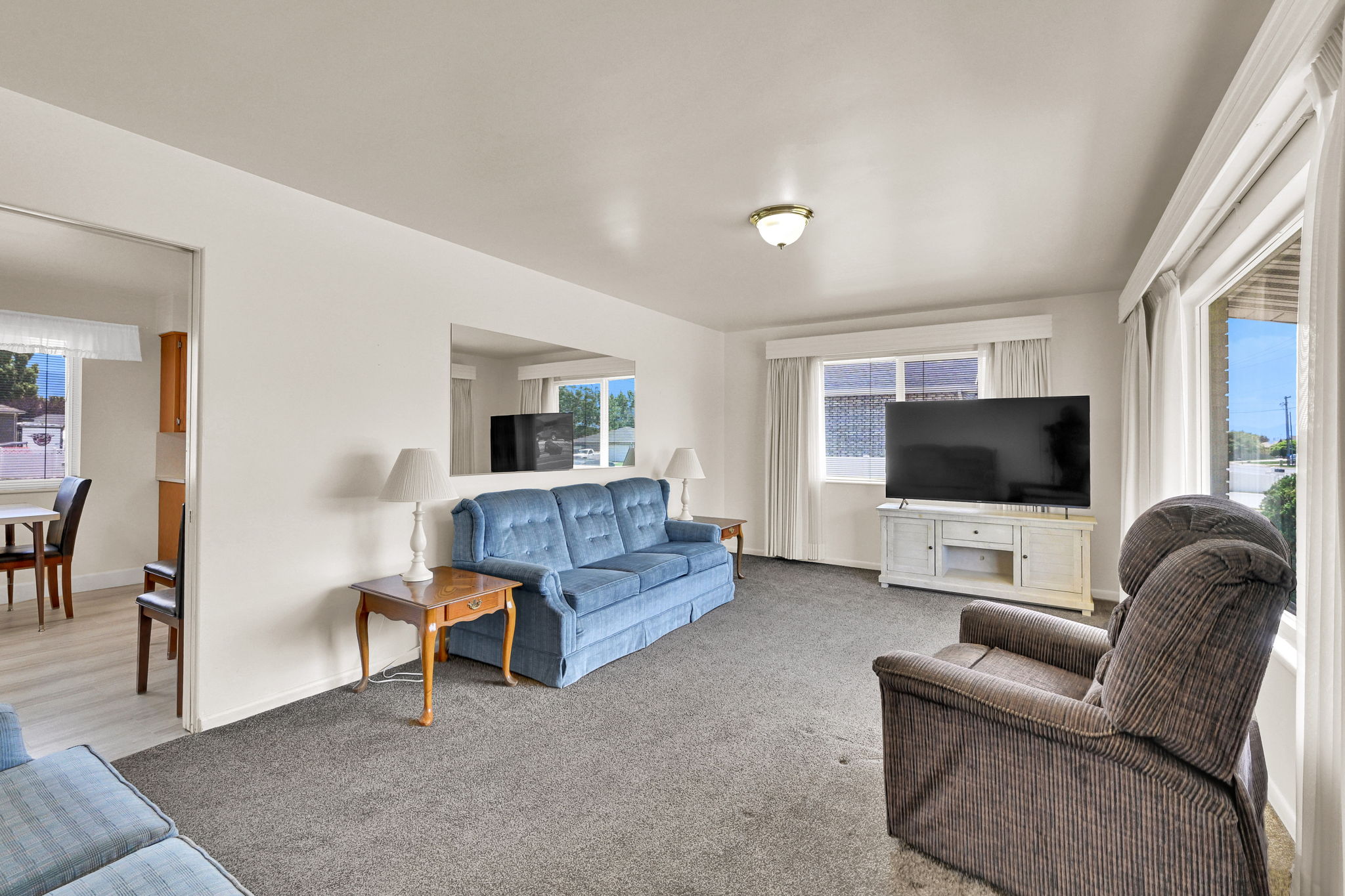 Spacious living area featuring neutral wall paint, gray carpeting, and multiple windows with white window treatments