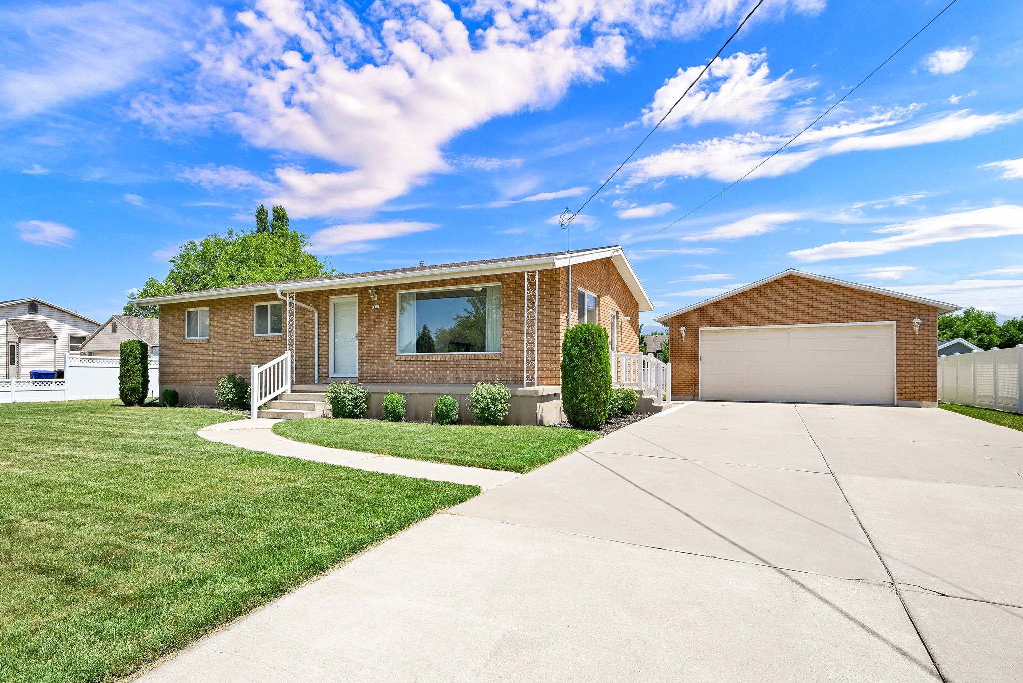 Brick exterior home featuring a concrete driveway, detached garage, and a manicured lawn