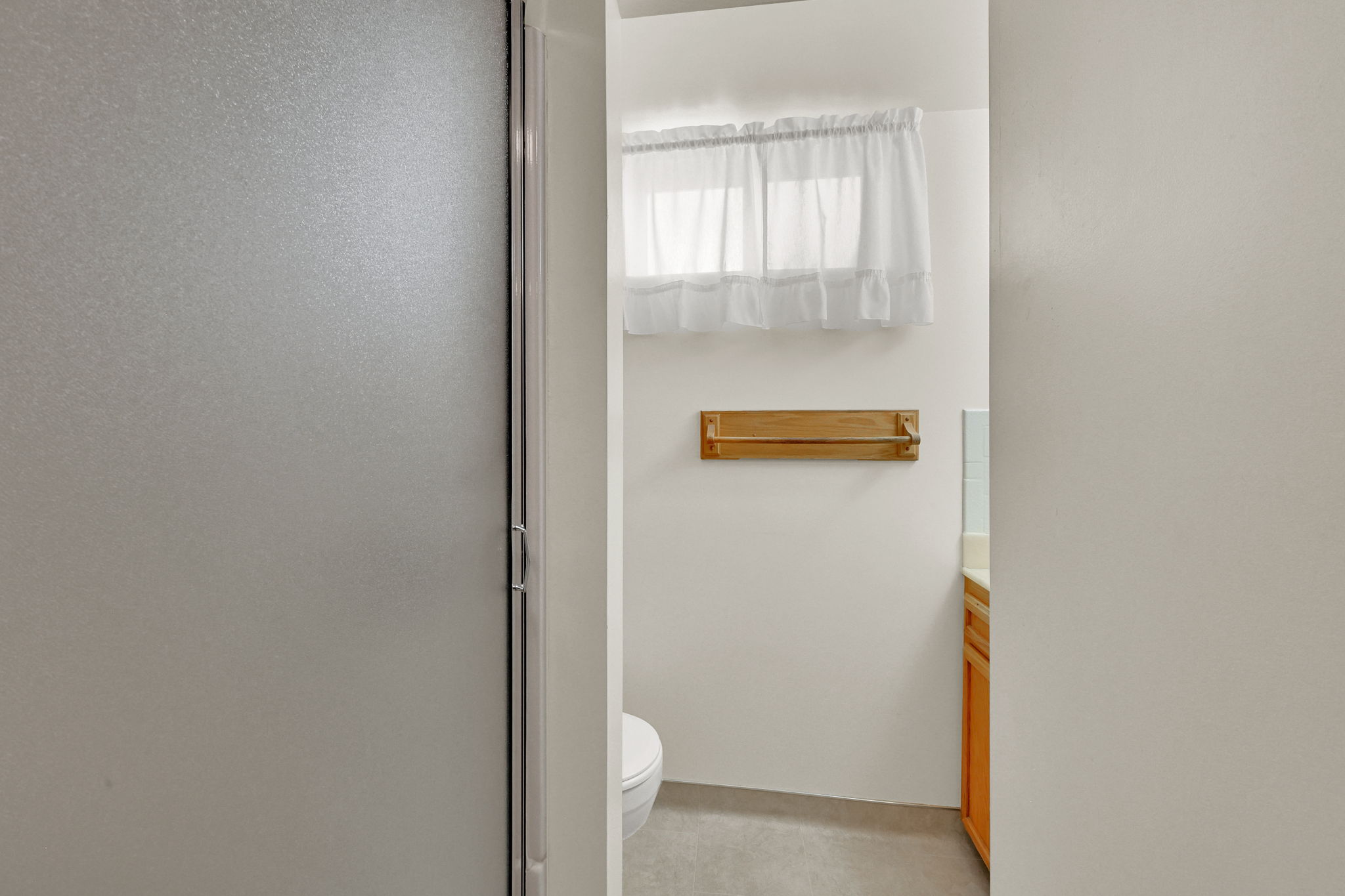 Frosted glass shower enclosure, white walls, and a small window featuring a white valance