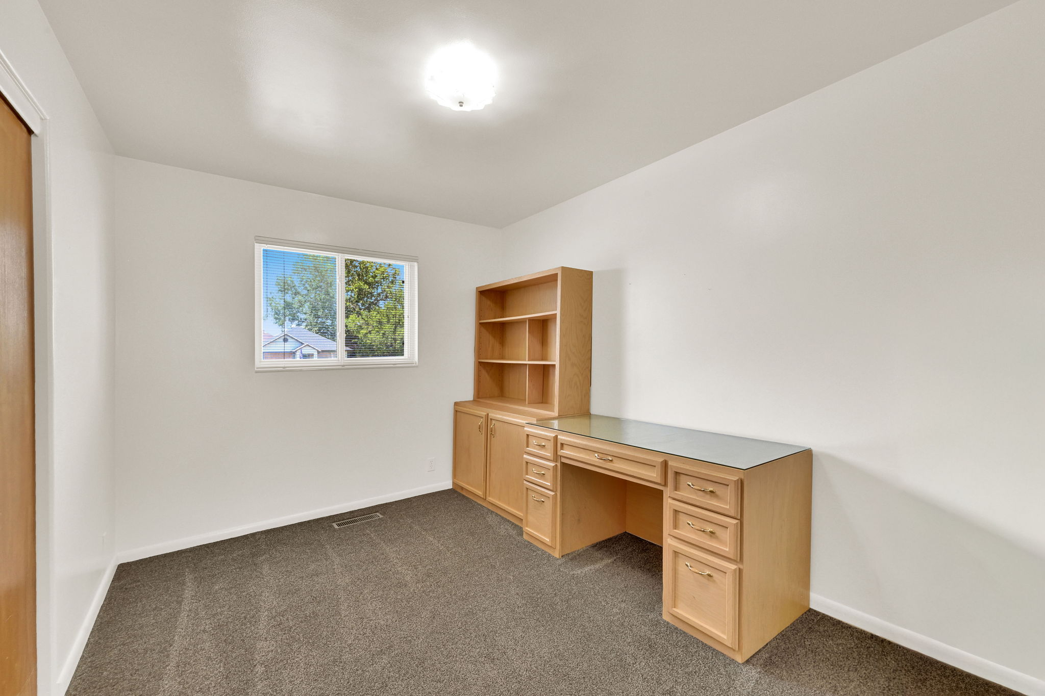 Built-in wood-finish desk with a glass top, integrated shelving, and cabinet storage