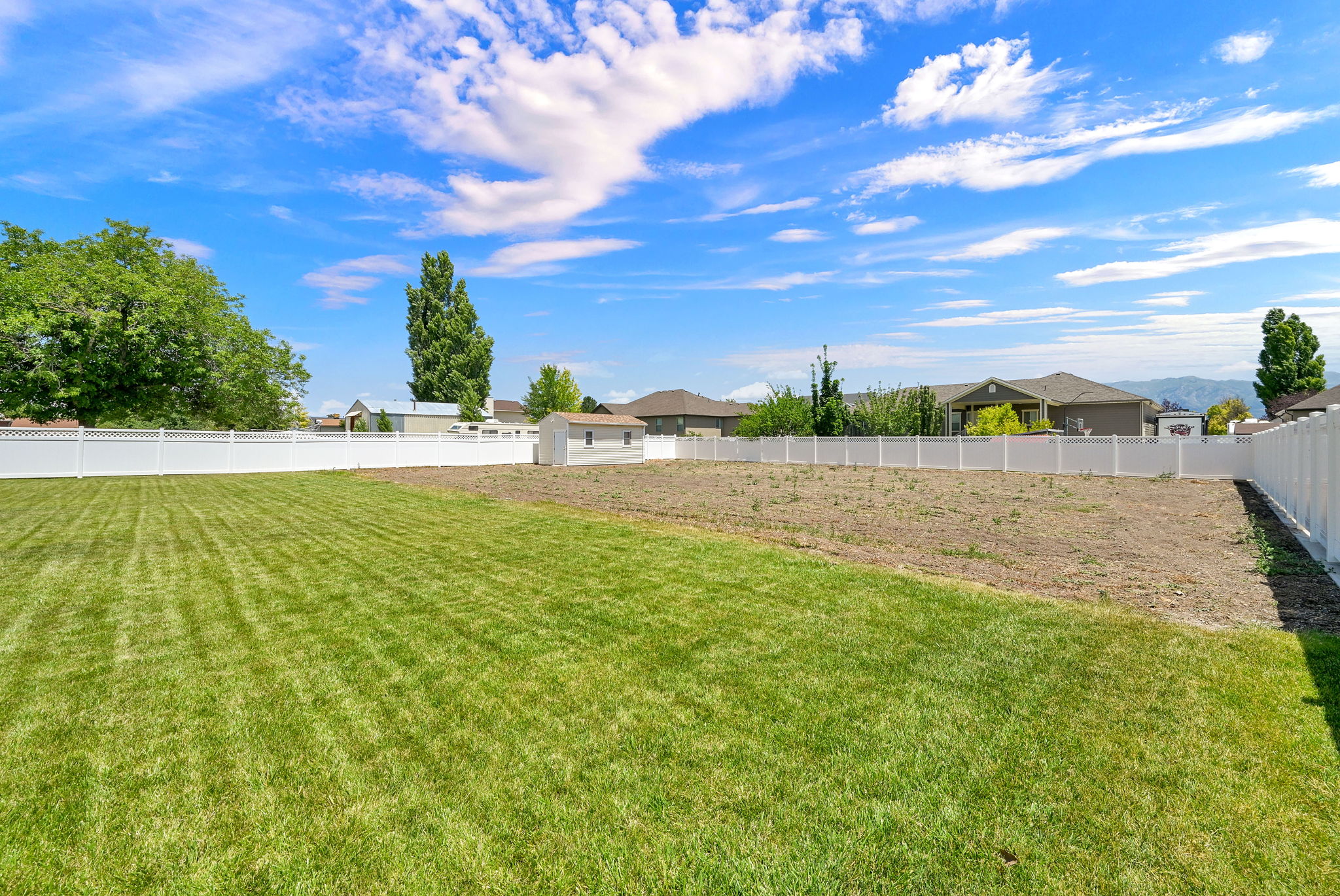 Expansive property featuring a vinyl privacy fence, a manicured lawn section, and an additional cleared area