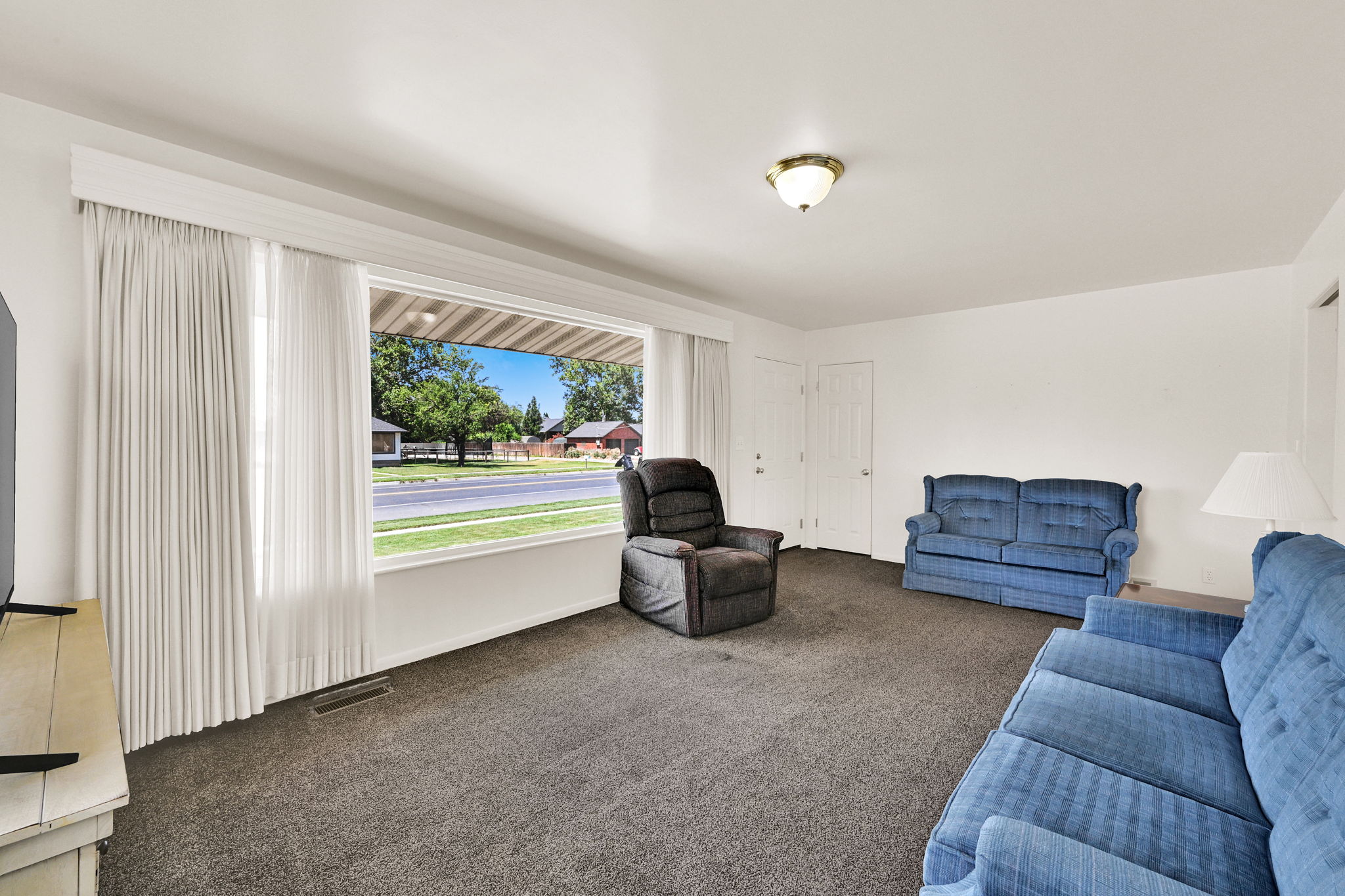 Spacious living area featuring a large picture window, neutral carpeting, white walls, and a ceiling-mounted light fixture
