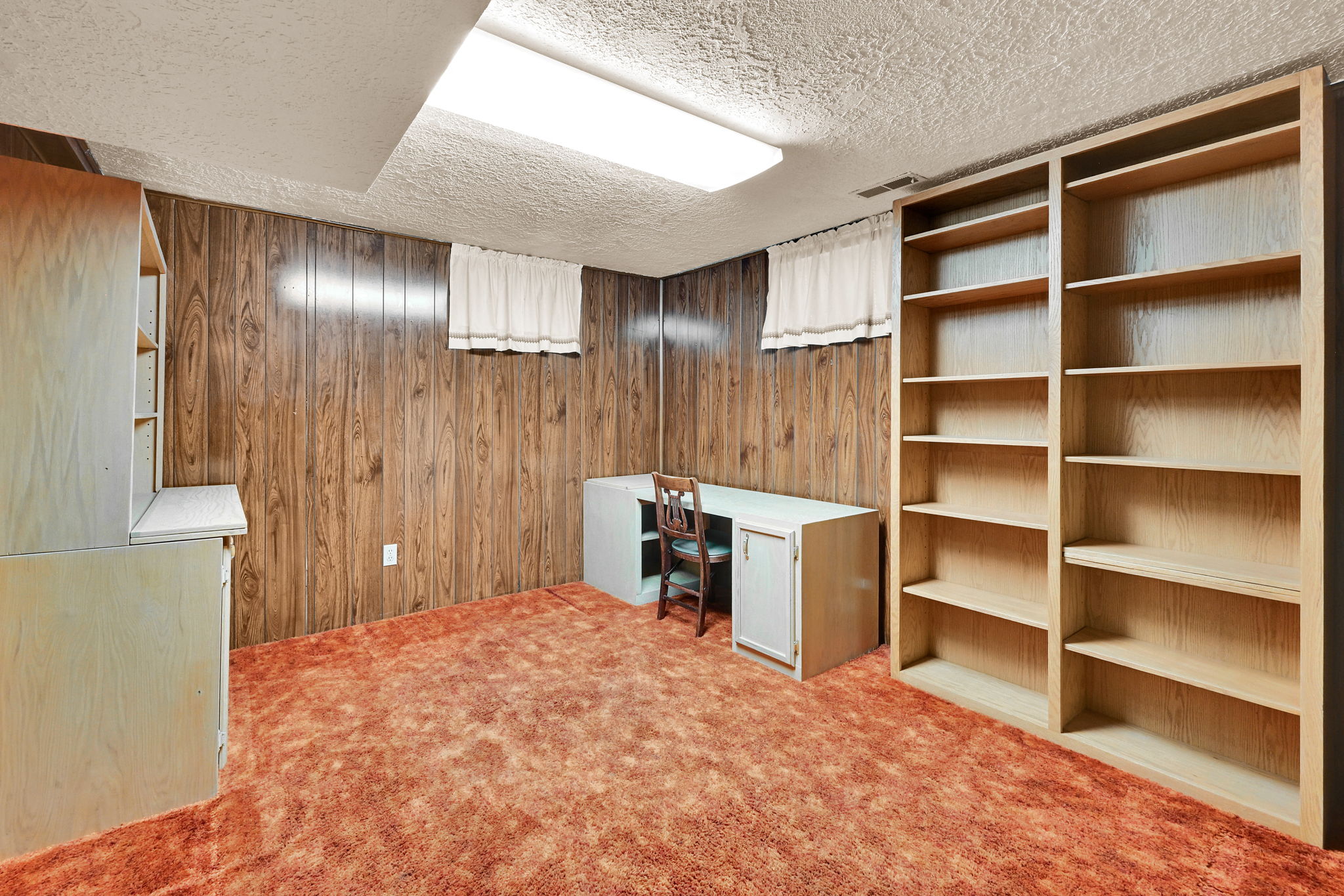 Room with wood-panel walls, built-in shelving, and carpet flooring