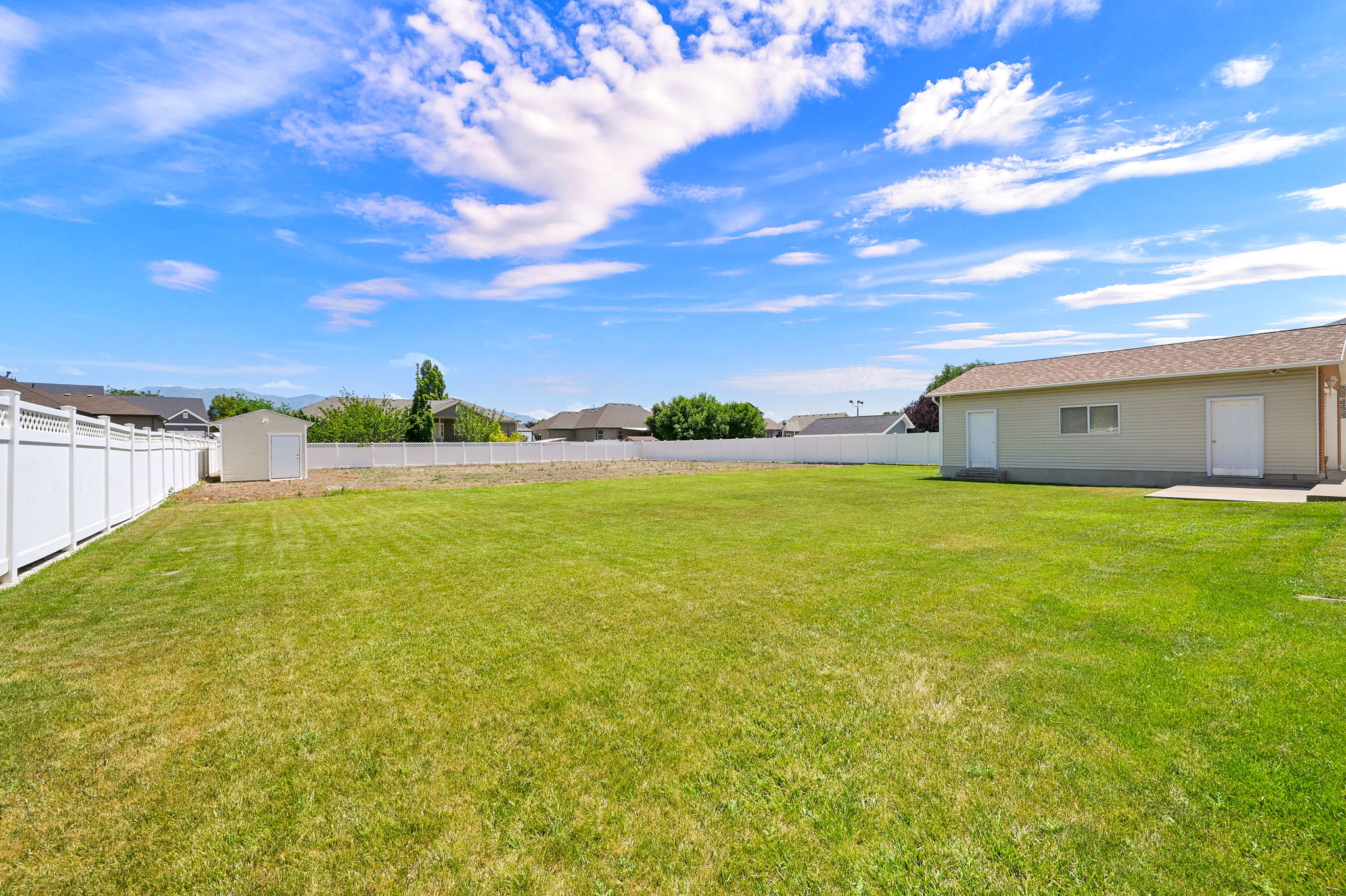Expansive grassy yard area featuring a detached auxiliary building, a separate storage shed, and durable white vinyl fencing