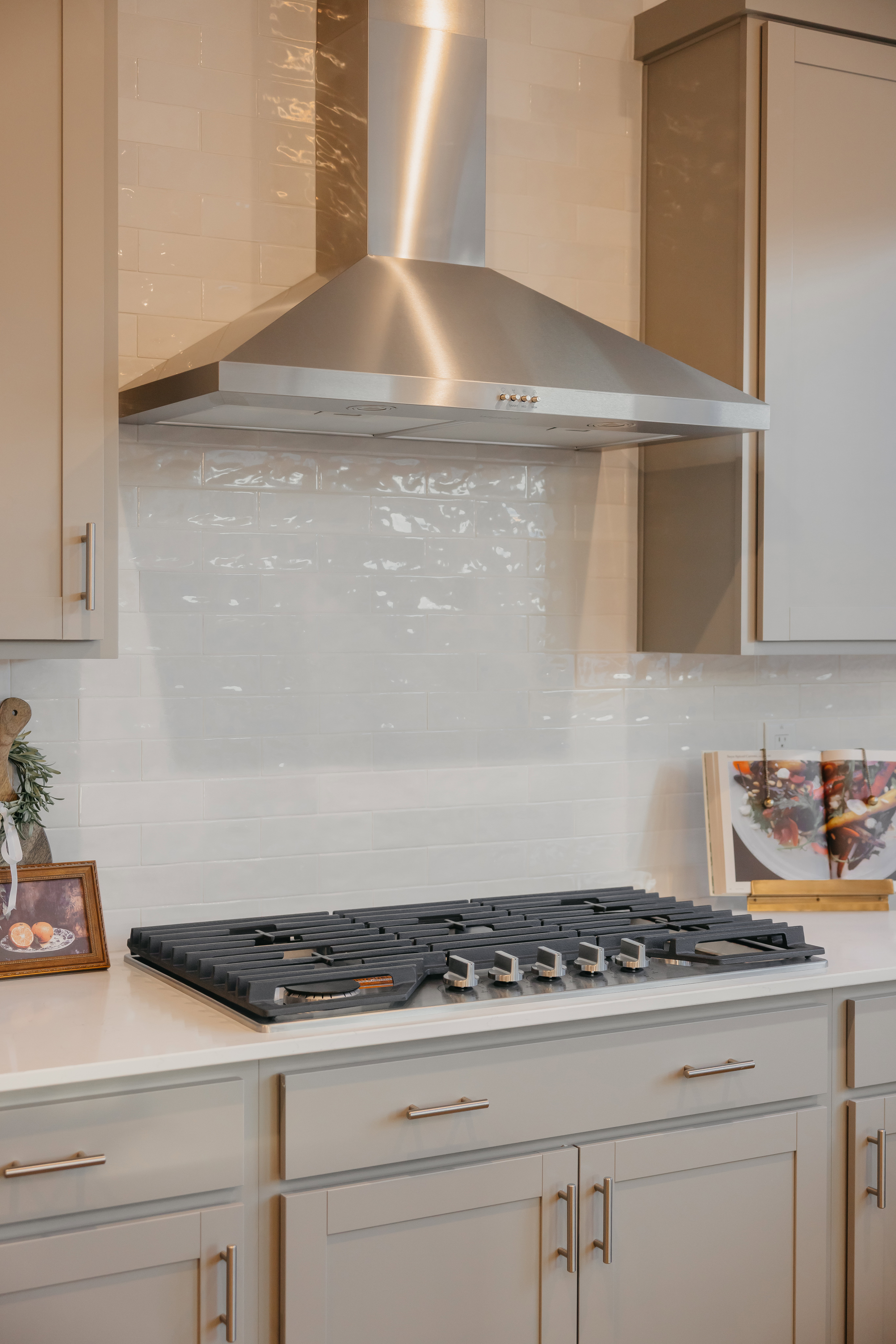 Stainless steel range hood over a gas cooktop, set against a white subway tile backsplash