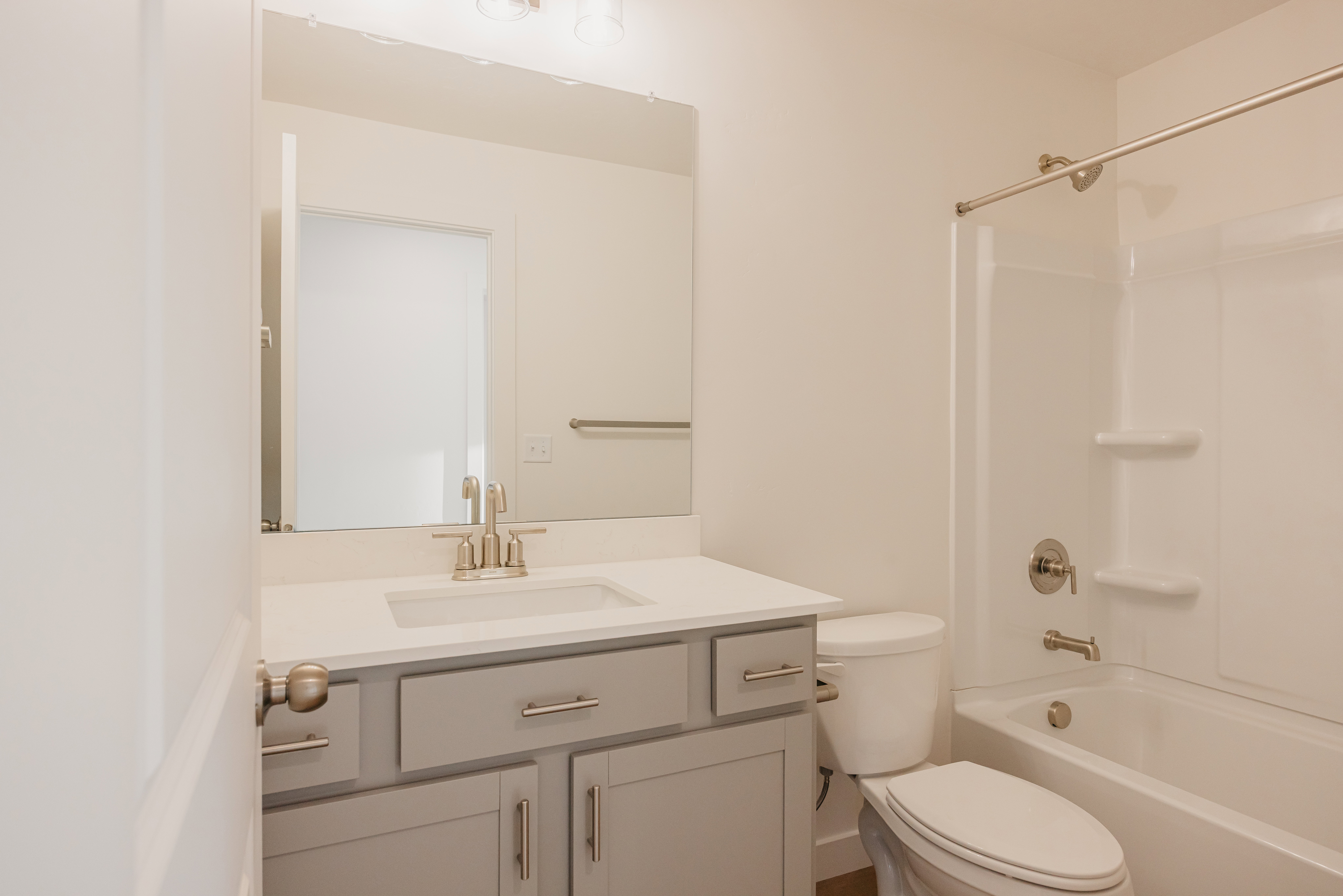 Bathroom featuring a light gray vanity with a white countertop and undermount sink, brushed nickel faucet, and a white tub with shower