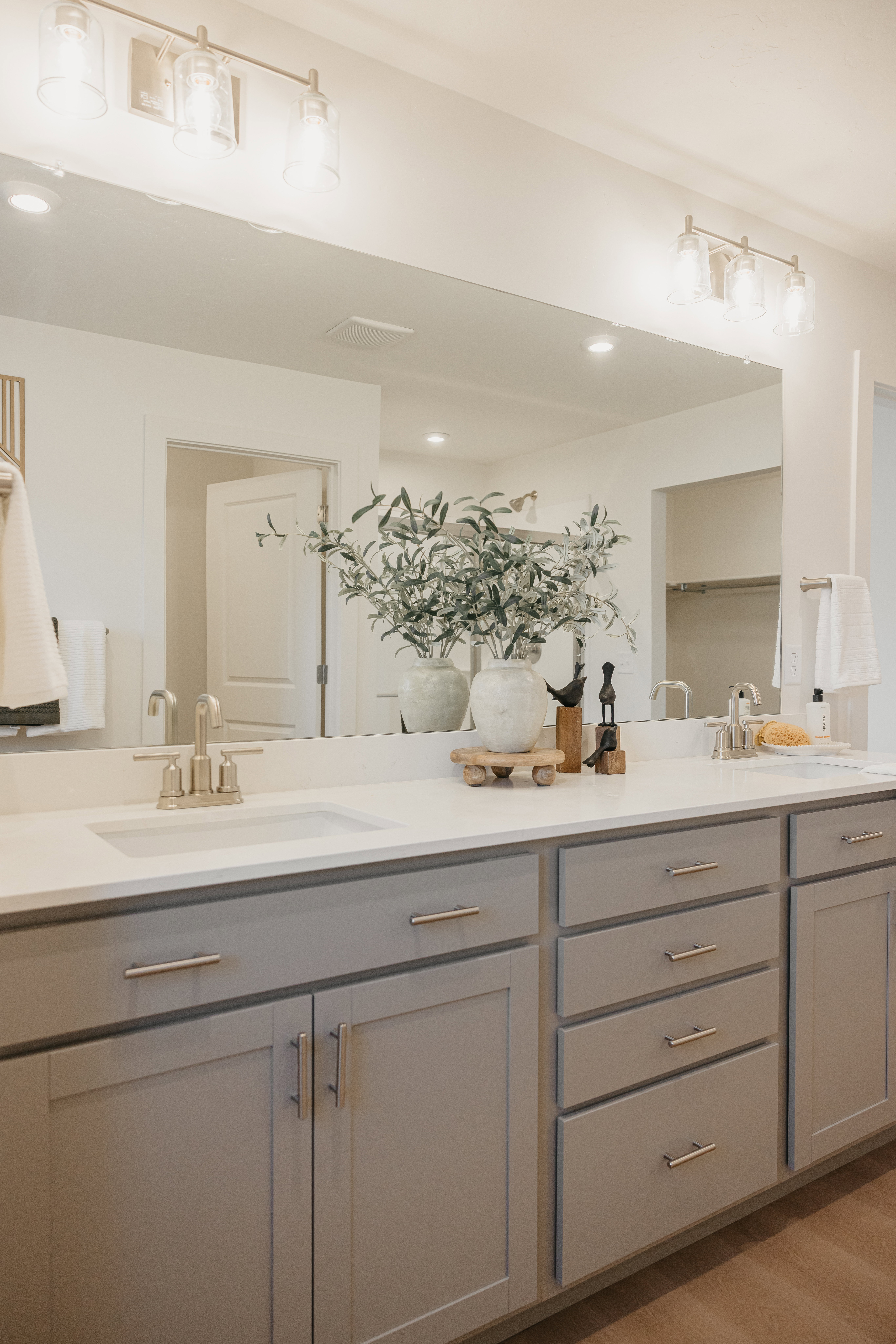 Dual vanity with light gray shaker-style cabinetry, chrome hardware, and white countertops