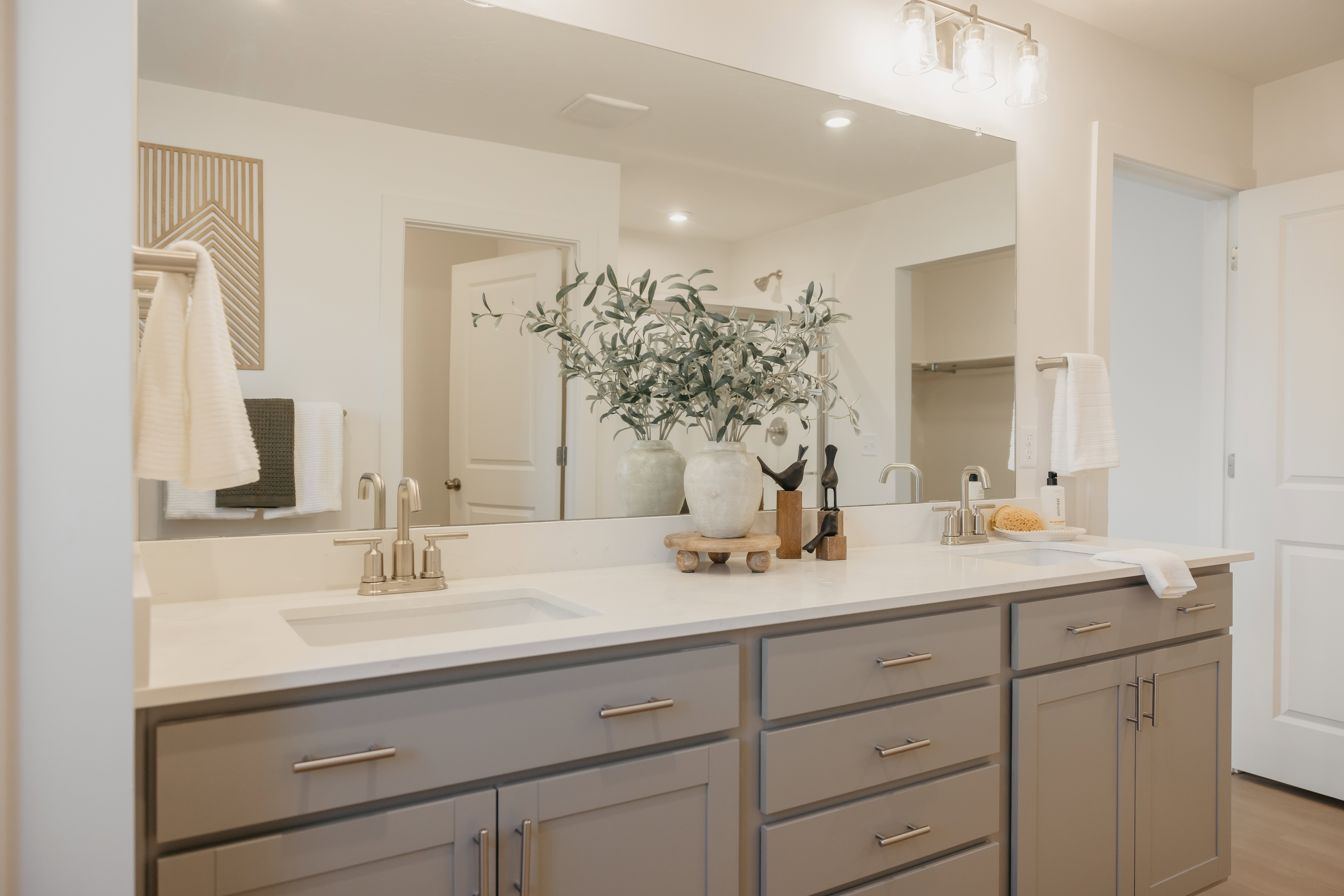 Spacious bathroom vanity featuring a double sink, light grey cabinetry, and a wide mirror with overhead lighting