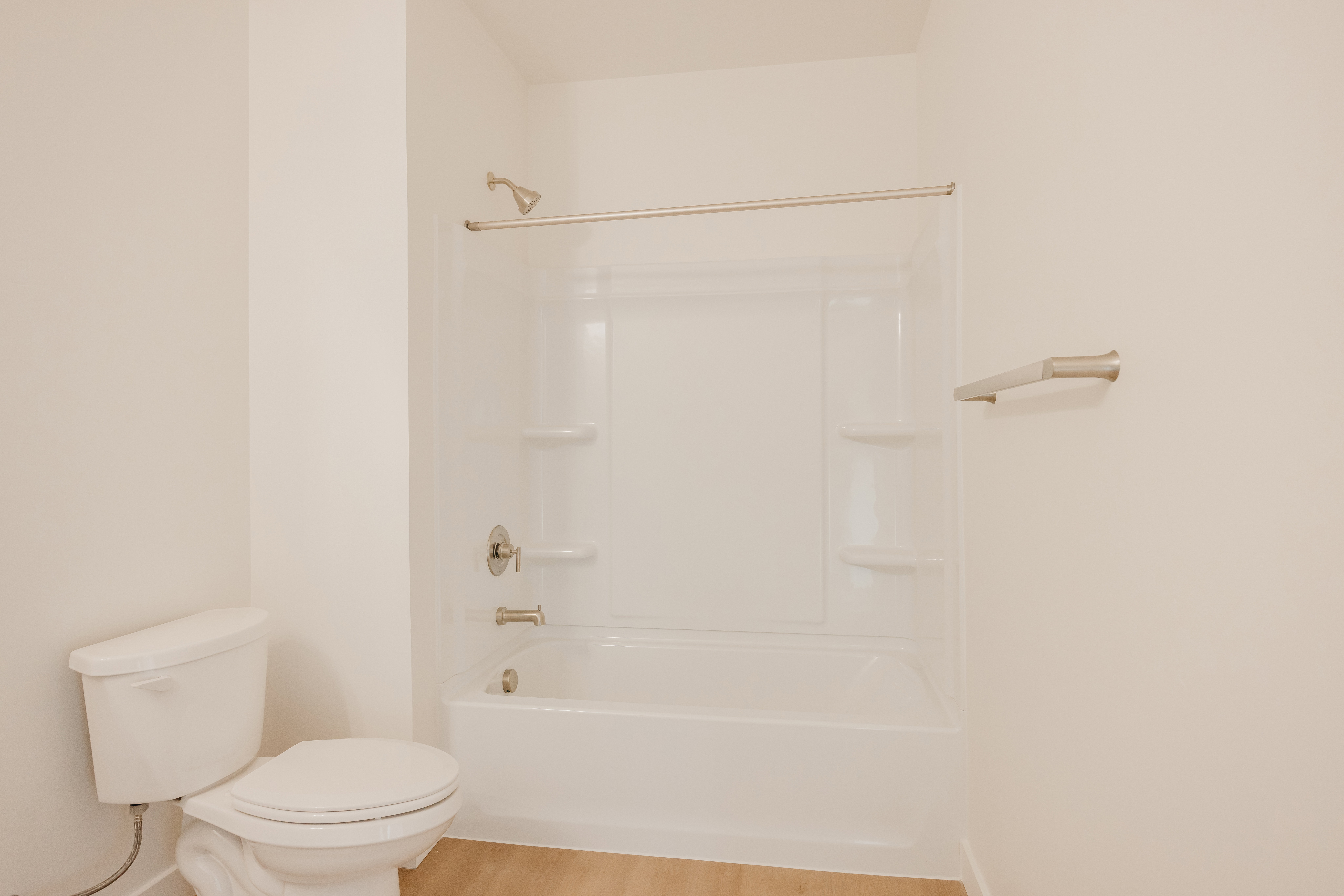 White bathtub and shower combination with integrated shelving, brushed nickel fixtures, and a coordinating towel bar
