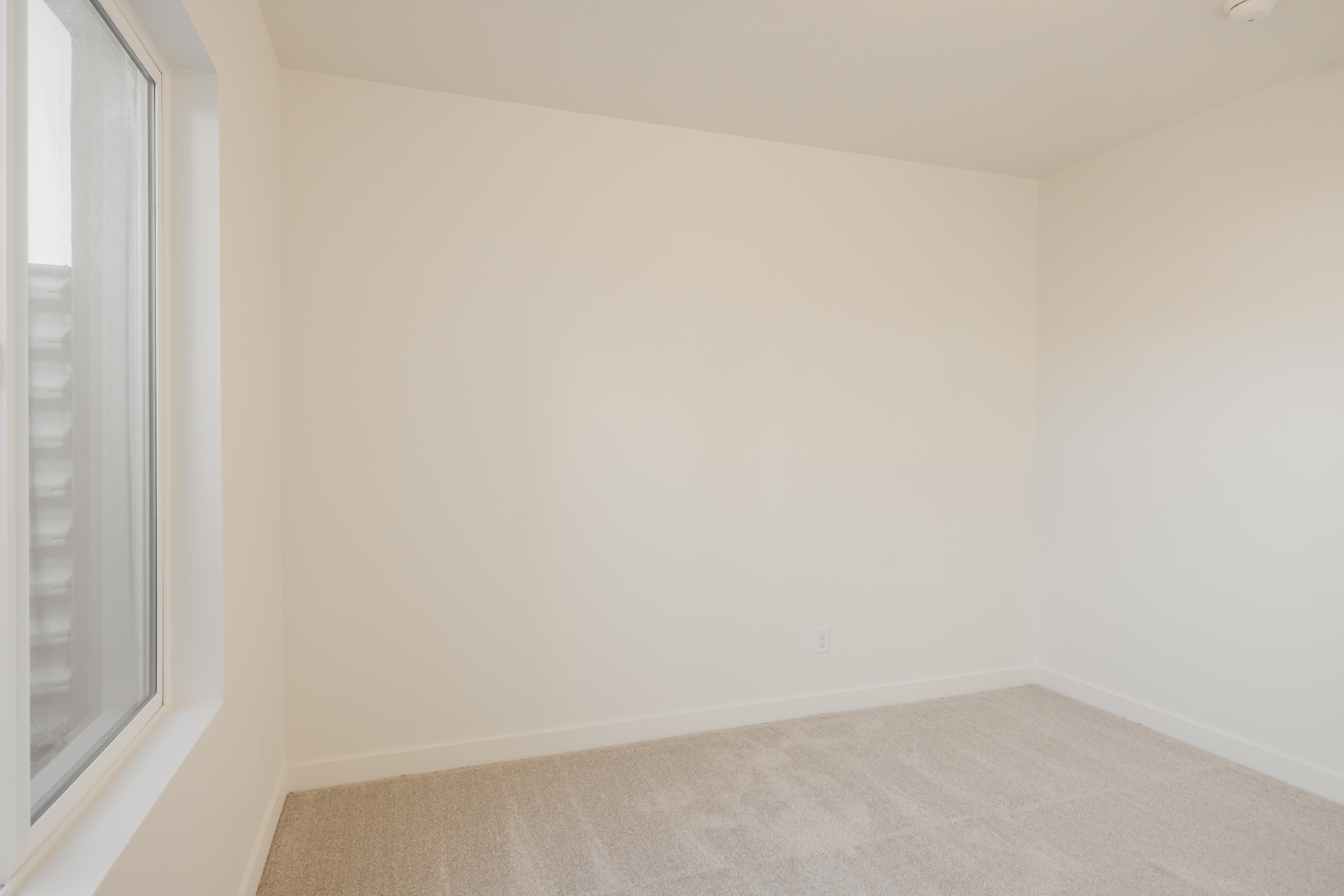 Neutral-toned room featuring a large window, light beige wall paint, white baseboards, and plush carpet flooring