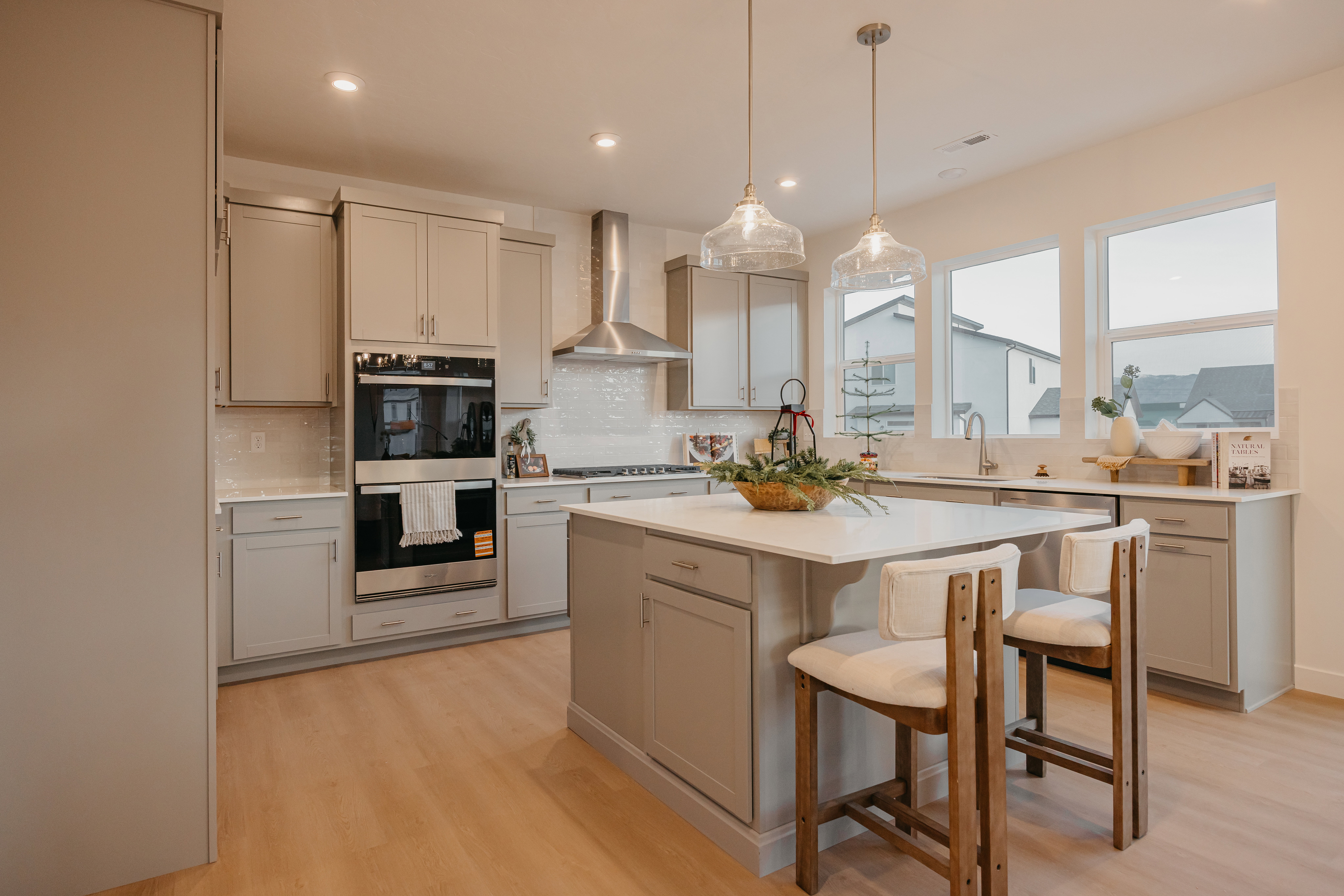 Spacious kitchen featuring an island with seating, light gray cabinetry, stainless steel appliances, wood-finish flooring, and multiple windows