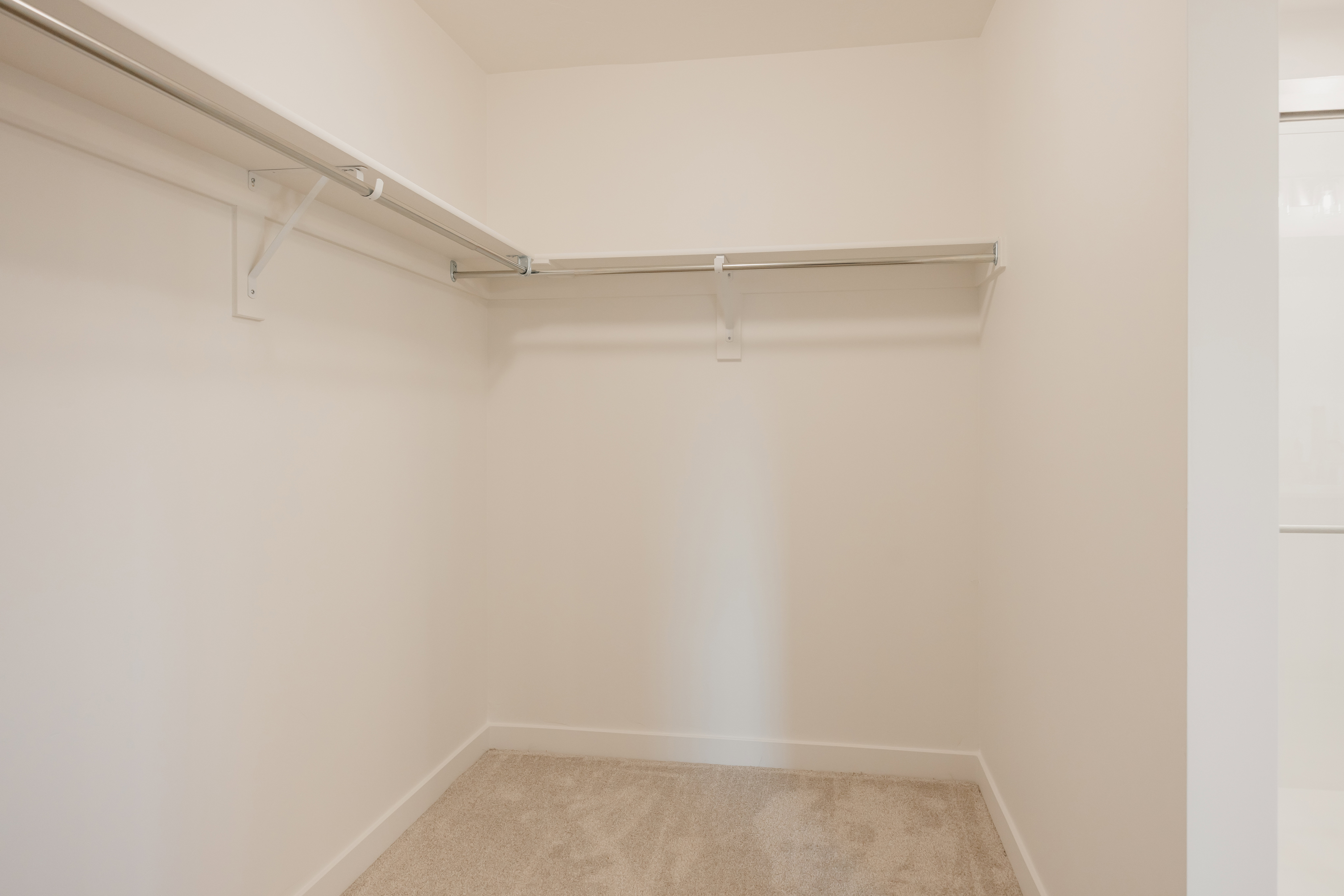 Walk-in closet featuring light-toned carpeting, white baseboards, and built-in metal shelving with hanging rods
