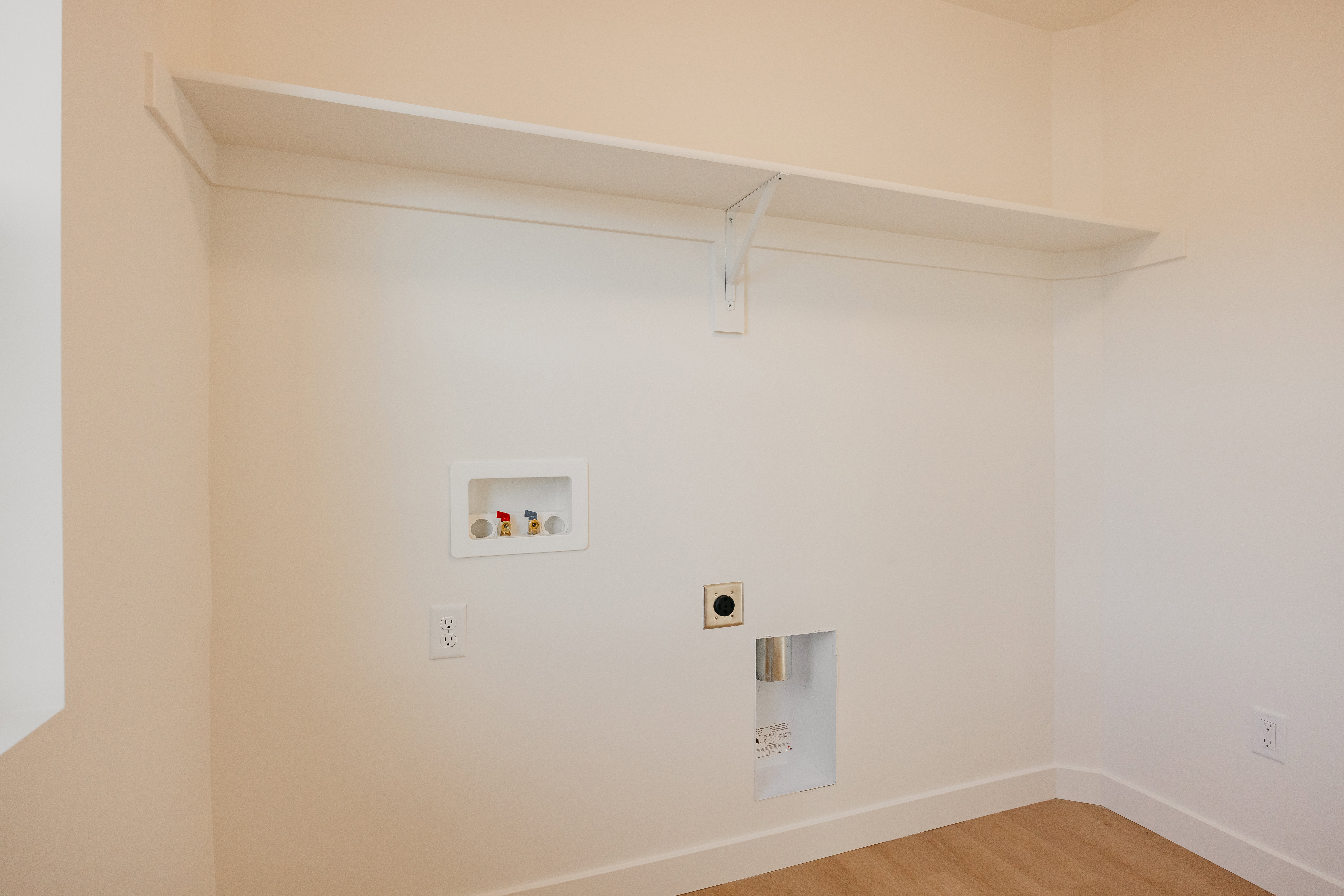 Dedicated laundry space featuring a white wall shelf, appliance hookups, and wood-finish flooring