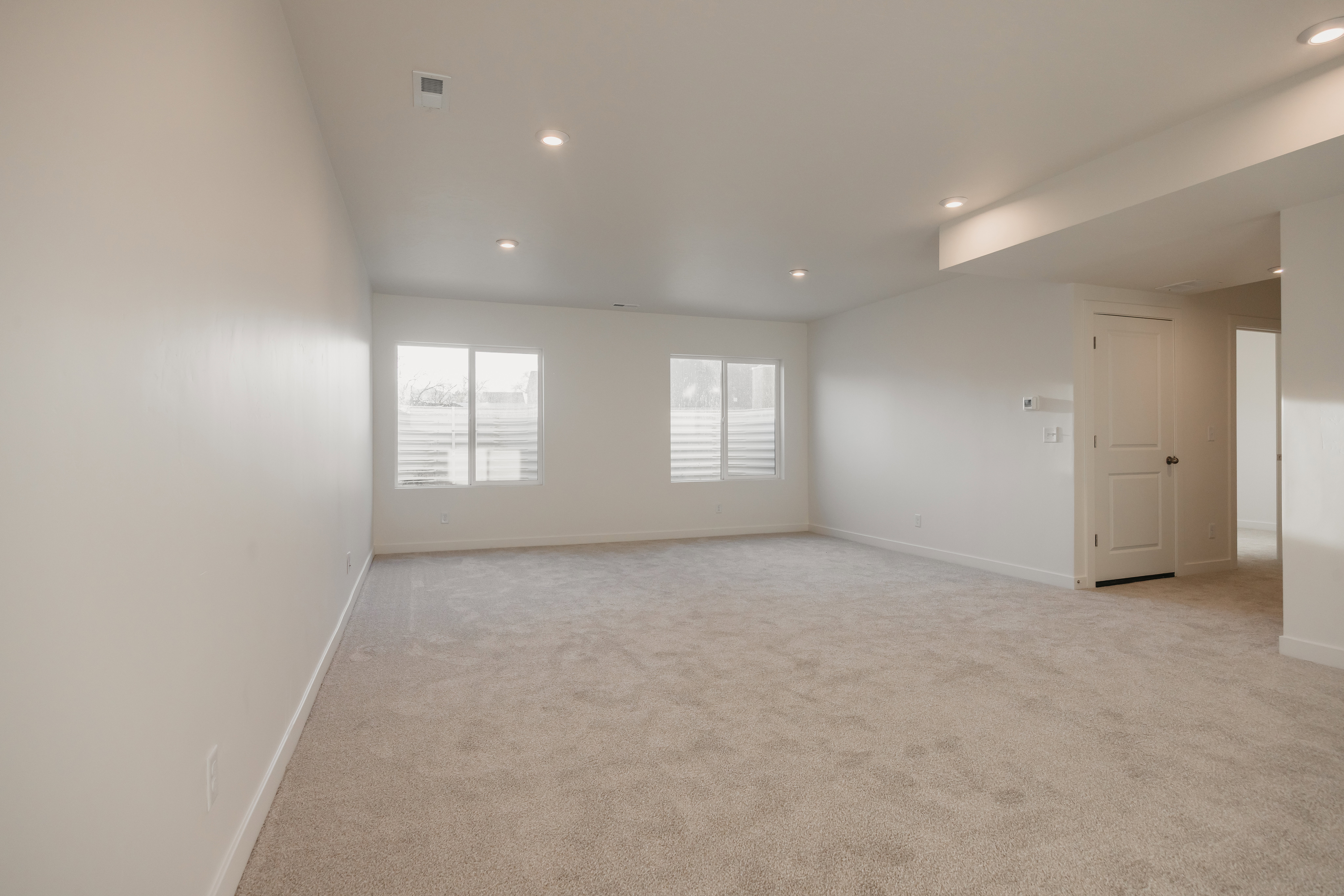 Spacious room featuring neutral carpet flooring, recessed lighting, white walls, and multiple windows with horizontal blinds