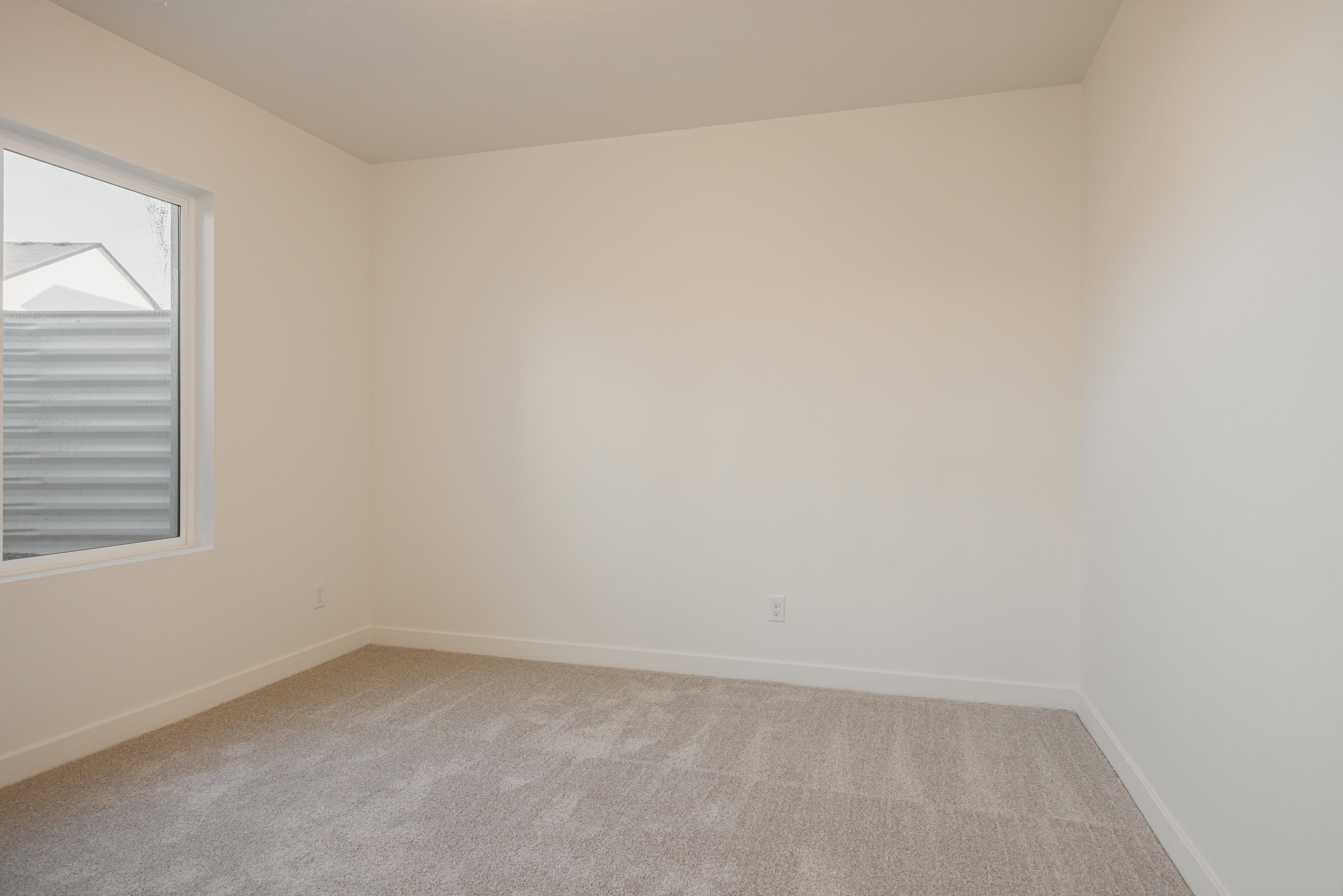 Light-filled room featuring neutral-toned carpet, white baseboards, and a large window with white trim