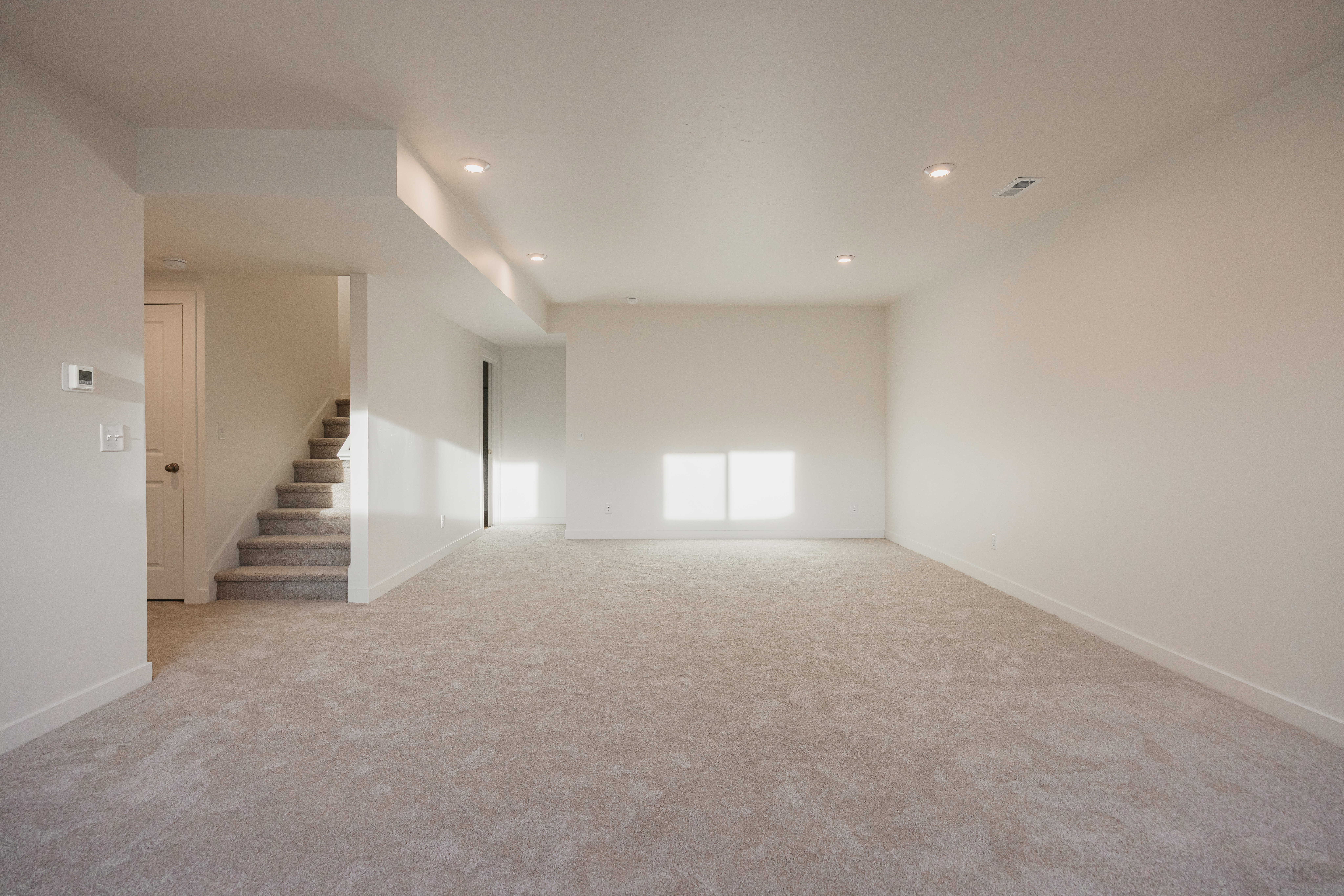 Spacious room featuring neutral carpeting, white baseboards, recessed lighting, and a staircase with matching neutral carpeting