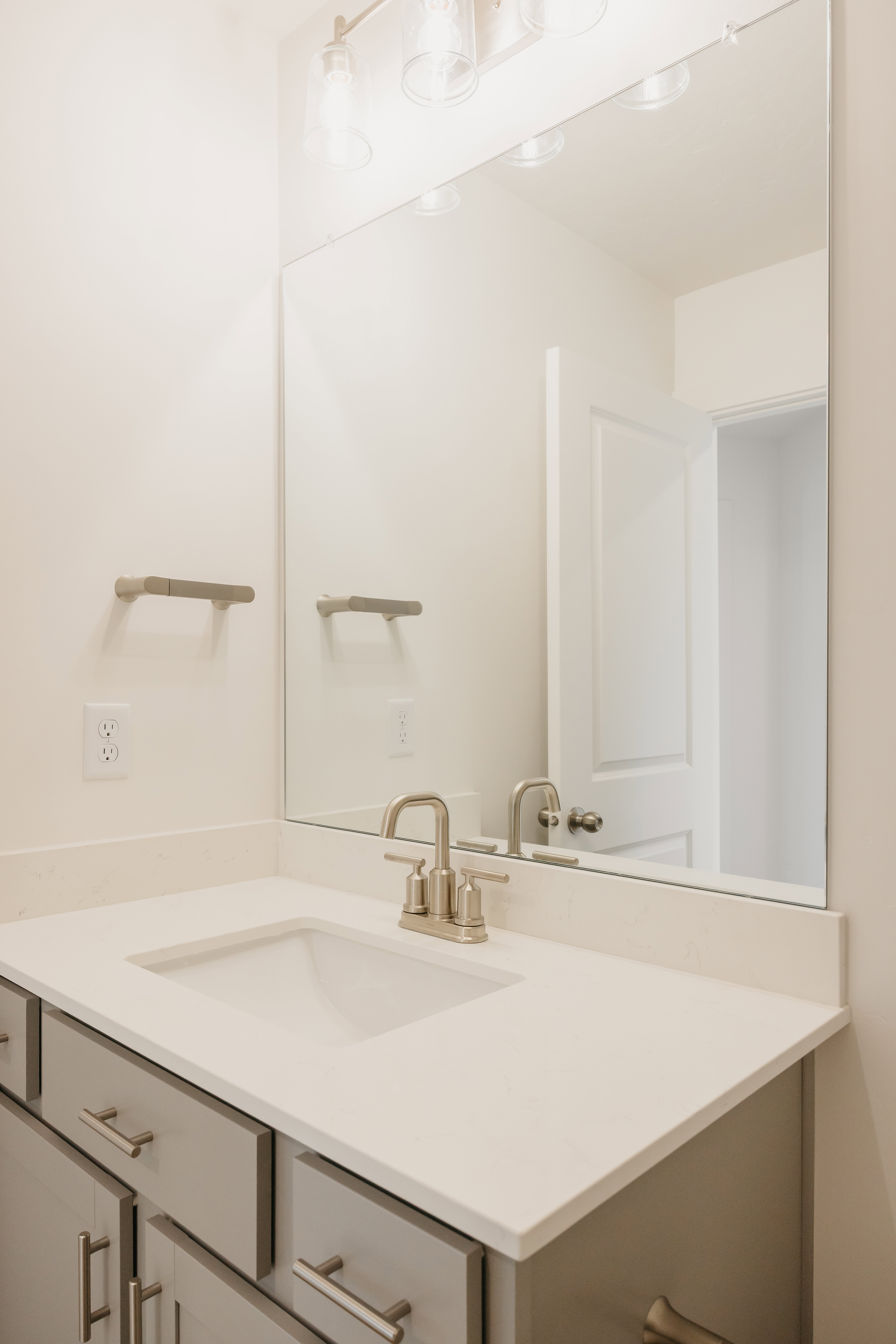 Bathroom vanity with a white countertop and integrated sink, brushed nickel faucet, and gray cabinetry with coordinating hardware