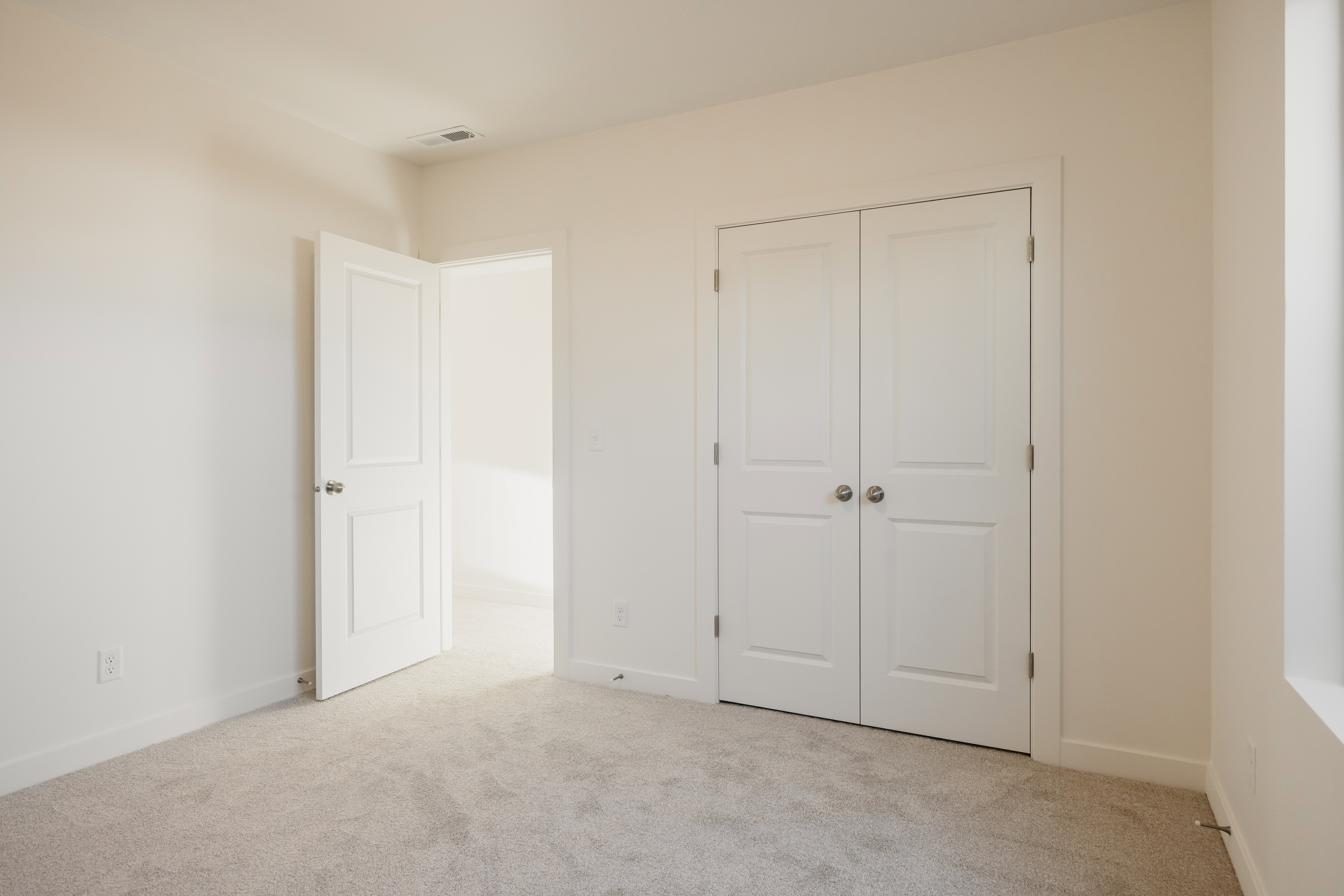 Neutral-toned room with plush carpet, featuring white paneled doors, polished chrome door hardware, and ample natural light from the window