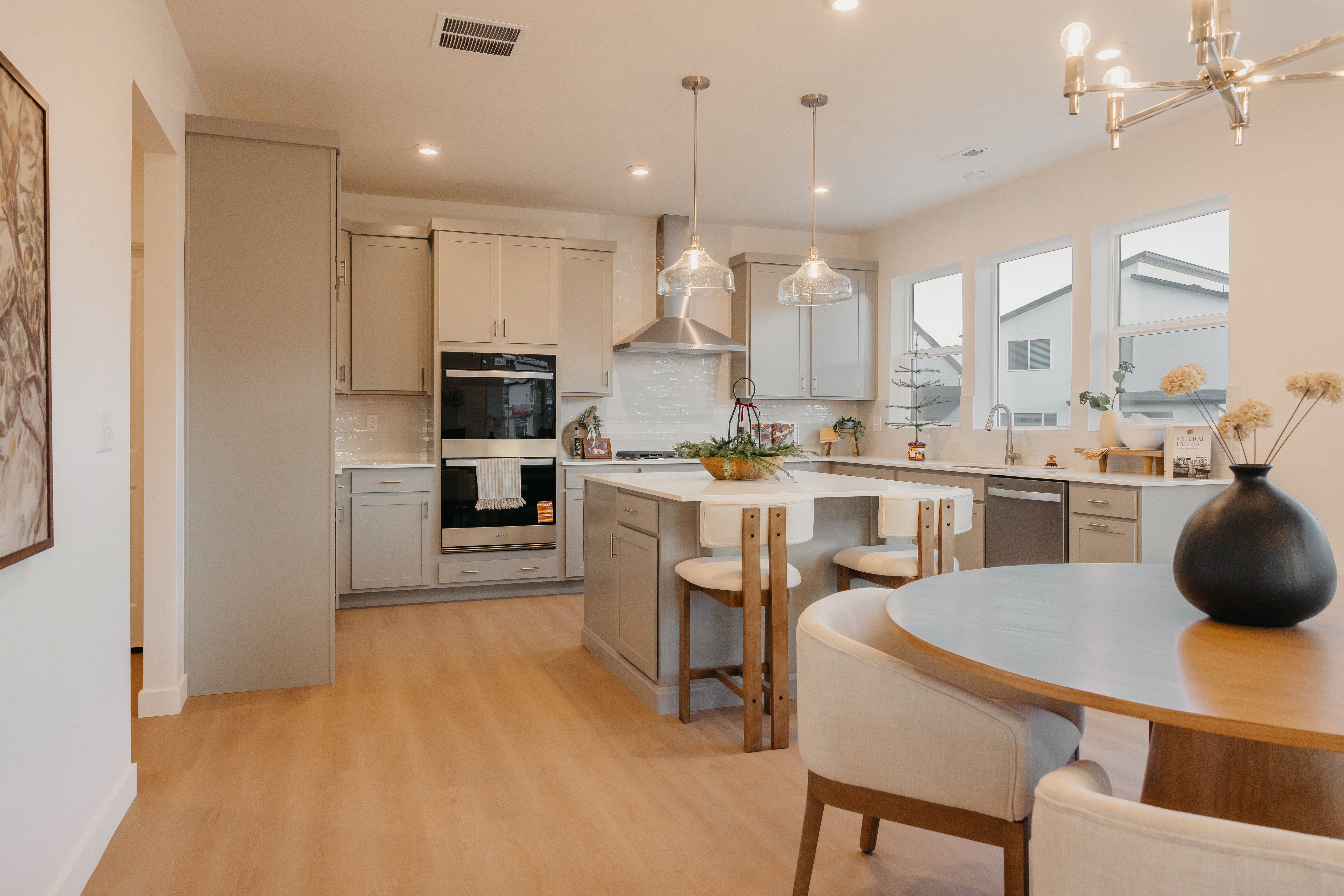 Modern kitchen featuring light wood-finish flooring, light grey cabinetry, stainless steel appliances, a center island with bar seating, and ample natural light from multiple windows