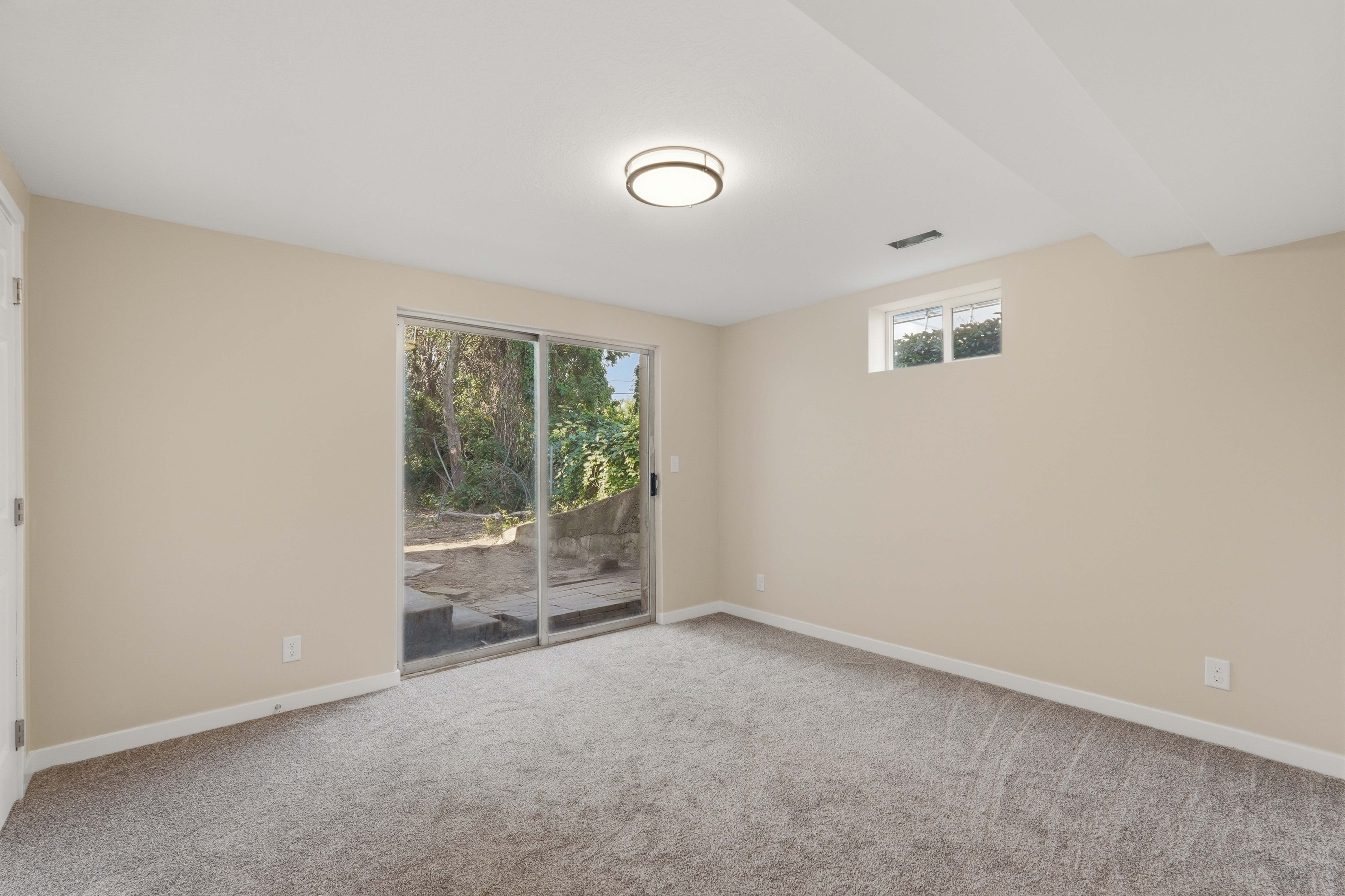 Spacious room featuring light beige walls, gray carpet flooring, and a contemporary flush-mount ceiling light
