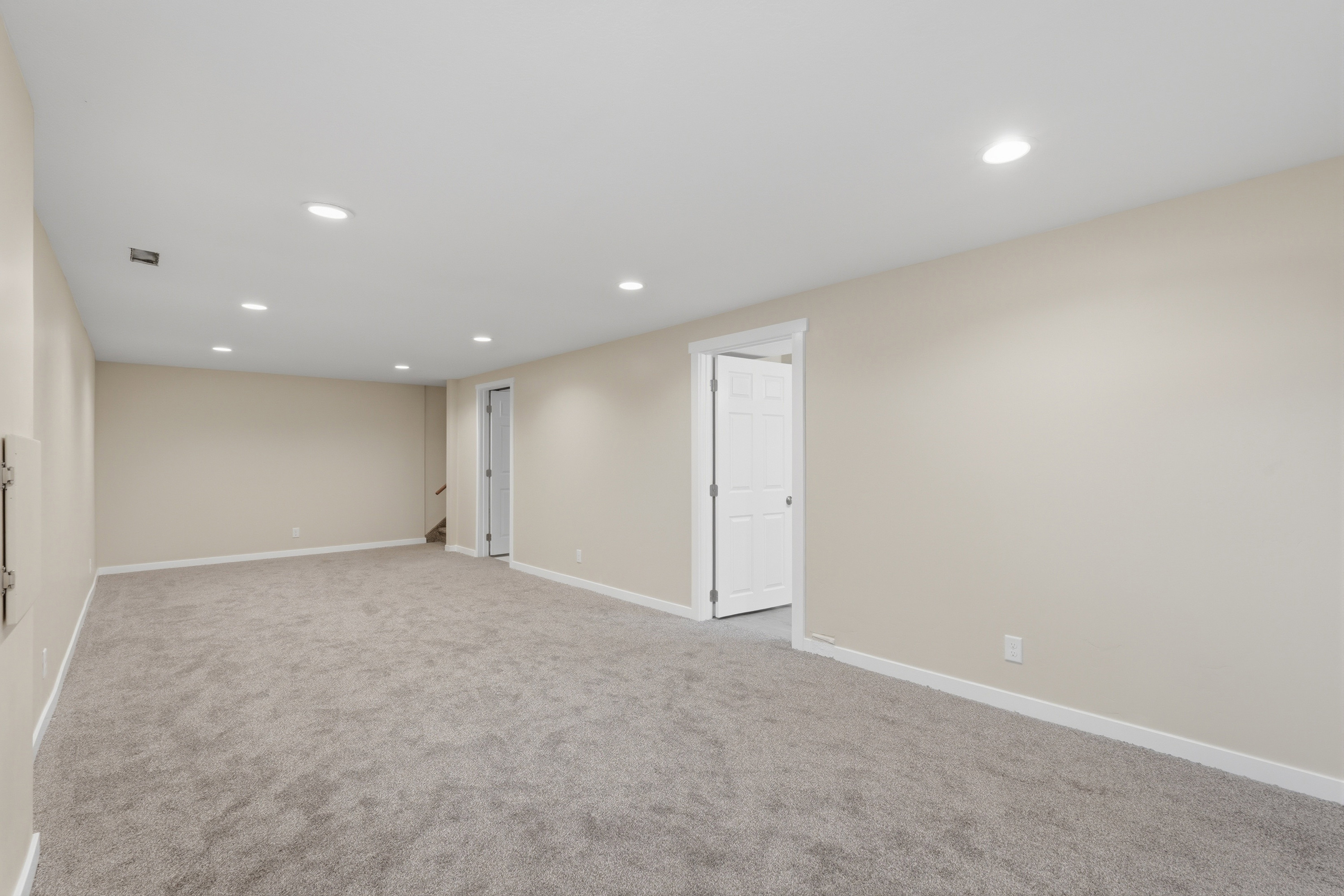 Spacious room featuring neutral carpeting, light-toned walls, recessed lighting, and white trim