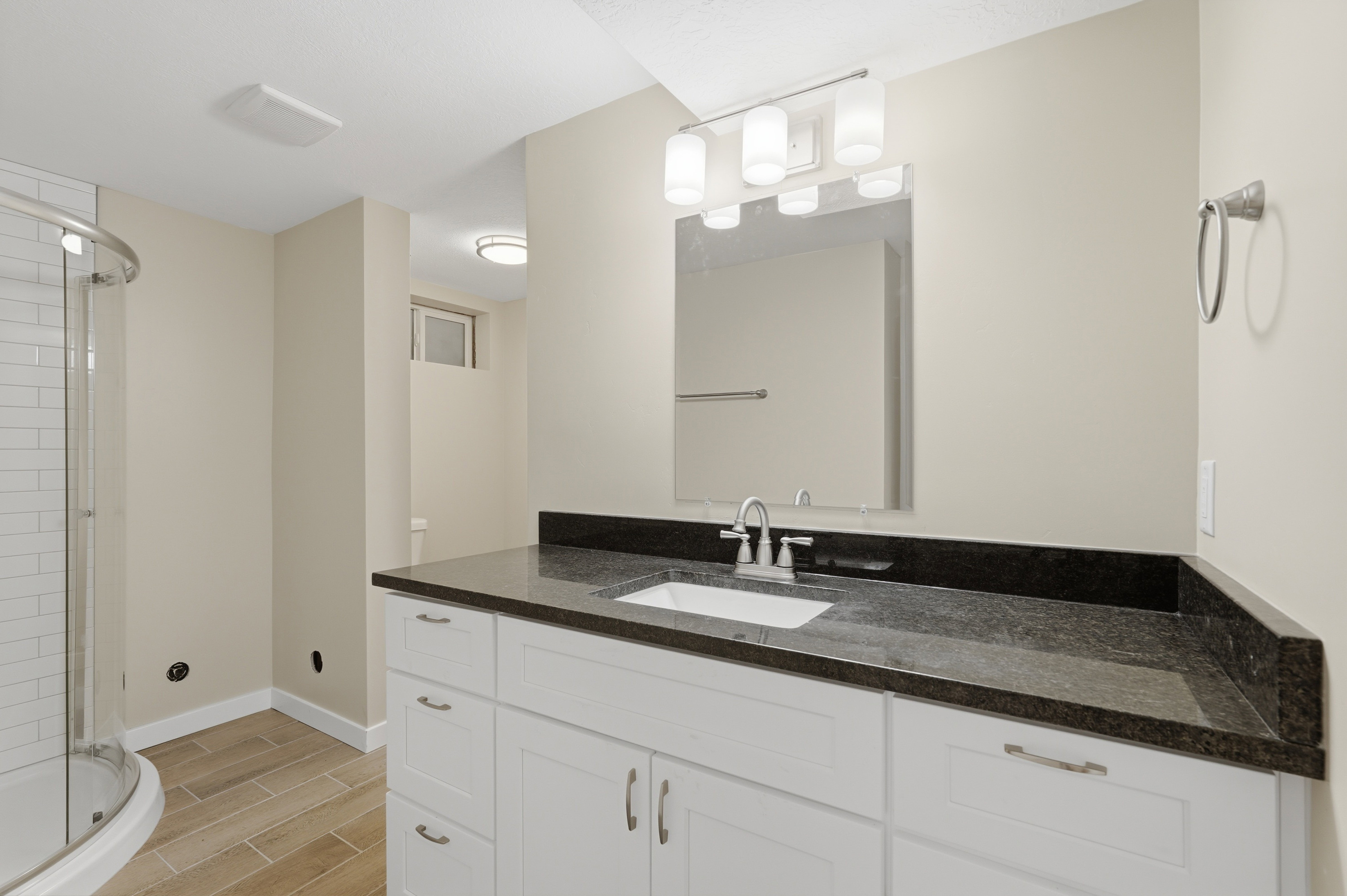 Bathroom featuring a white vanity with brushed nickel hardware, dark stone countertop, undermount sink, and a framed mirror with a four-light fixture
