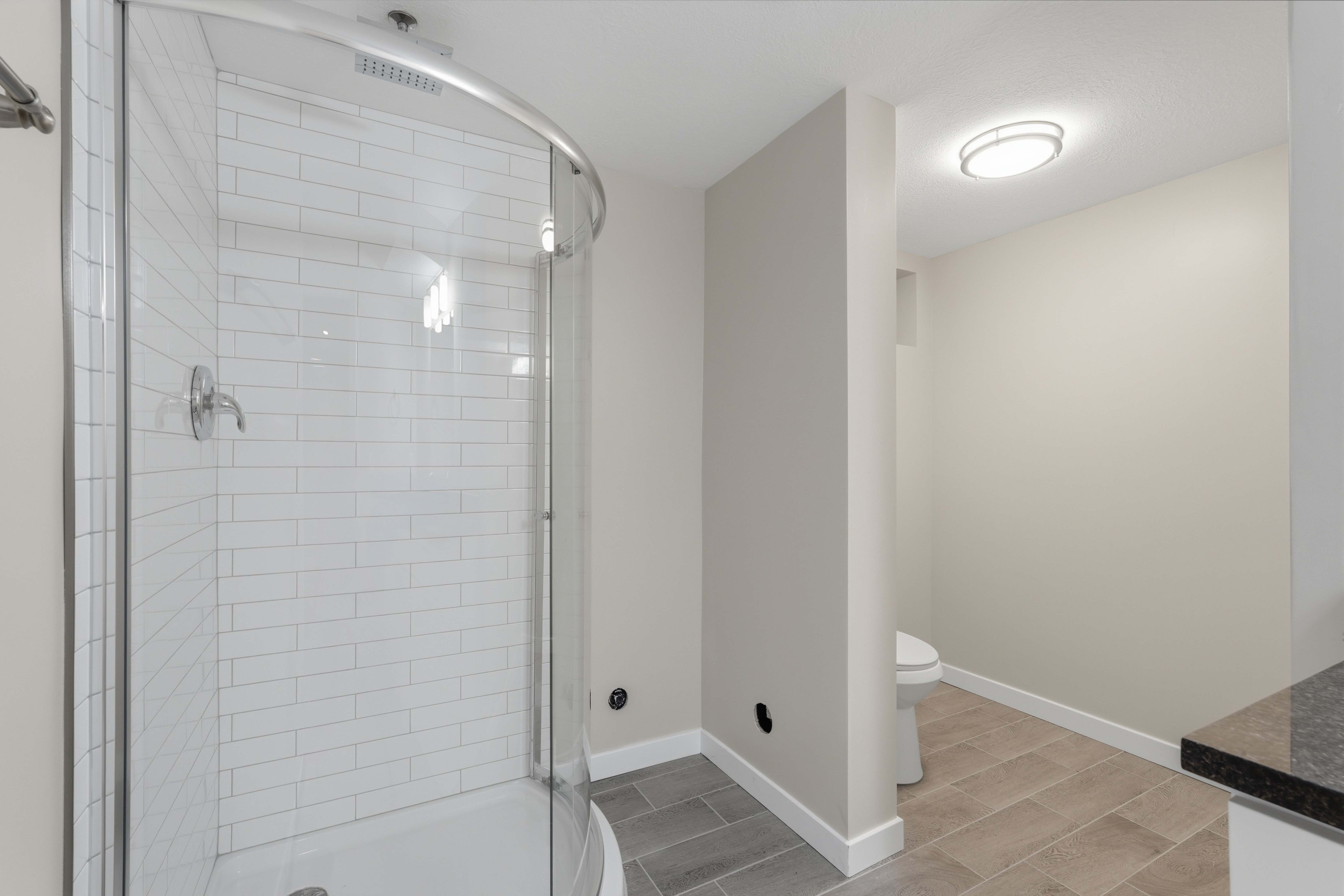 Curved glass shower enclosure with subway tile surround and chrome fixtures
