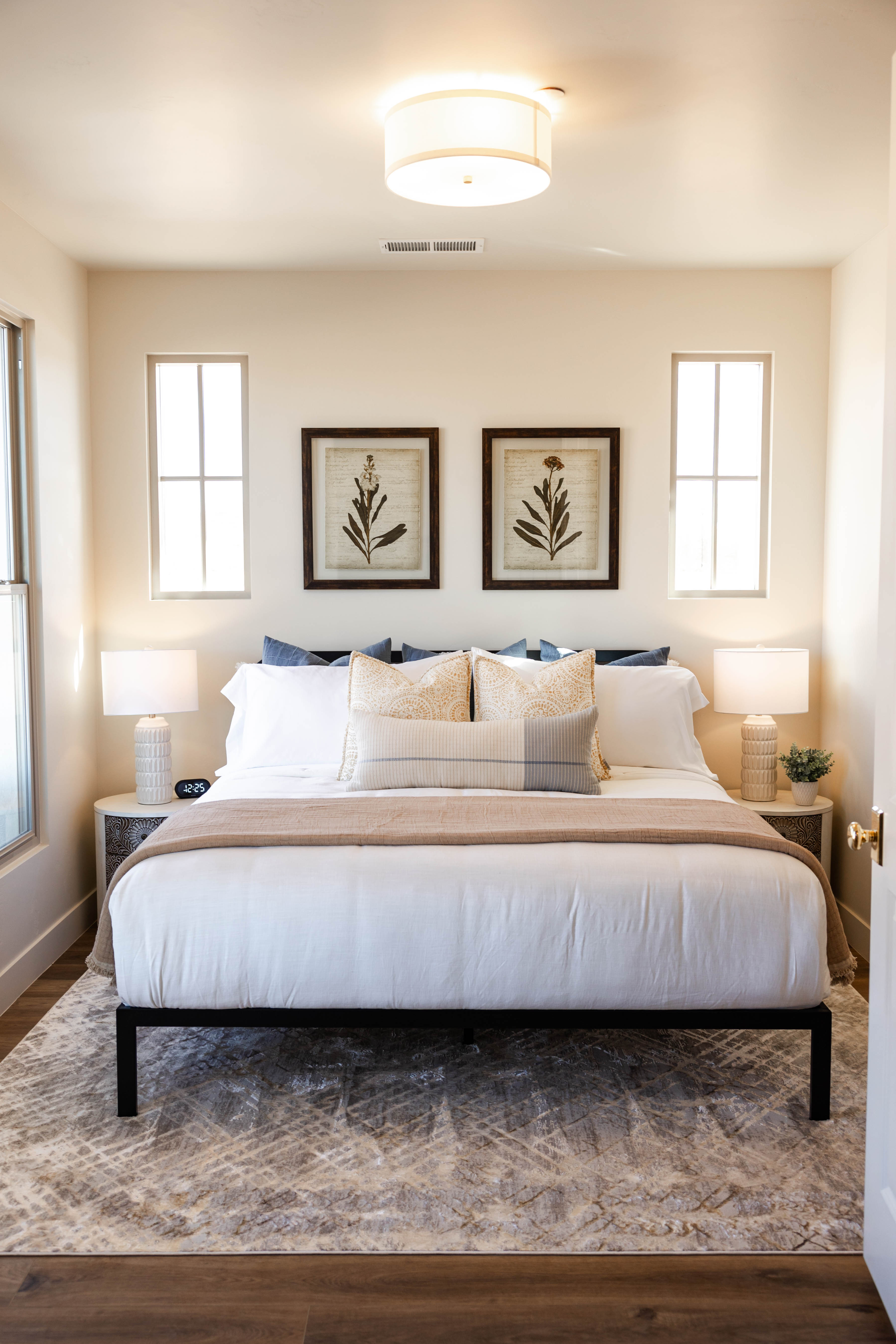 Bedroom featuring wood-finish flooring, two vertical windowpanes, a flush-mount ceiling light fixture, and light-toned walls