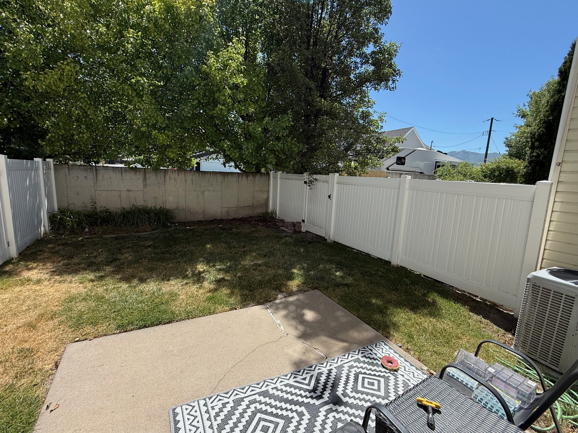 Private backyard space featuring a concrete patio, a section of lawn, and a white privacy fence with a gate