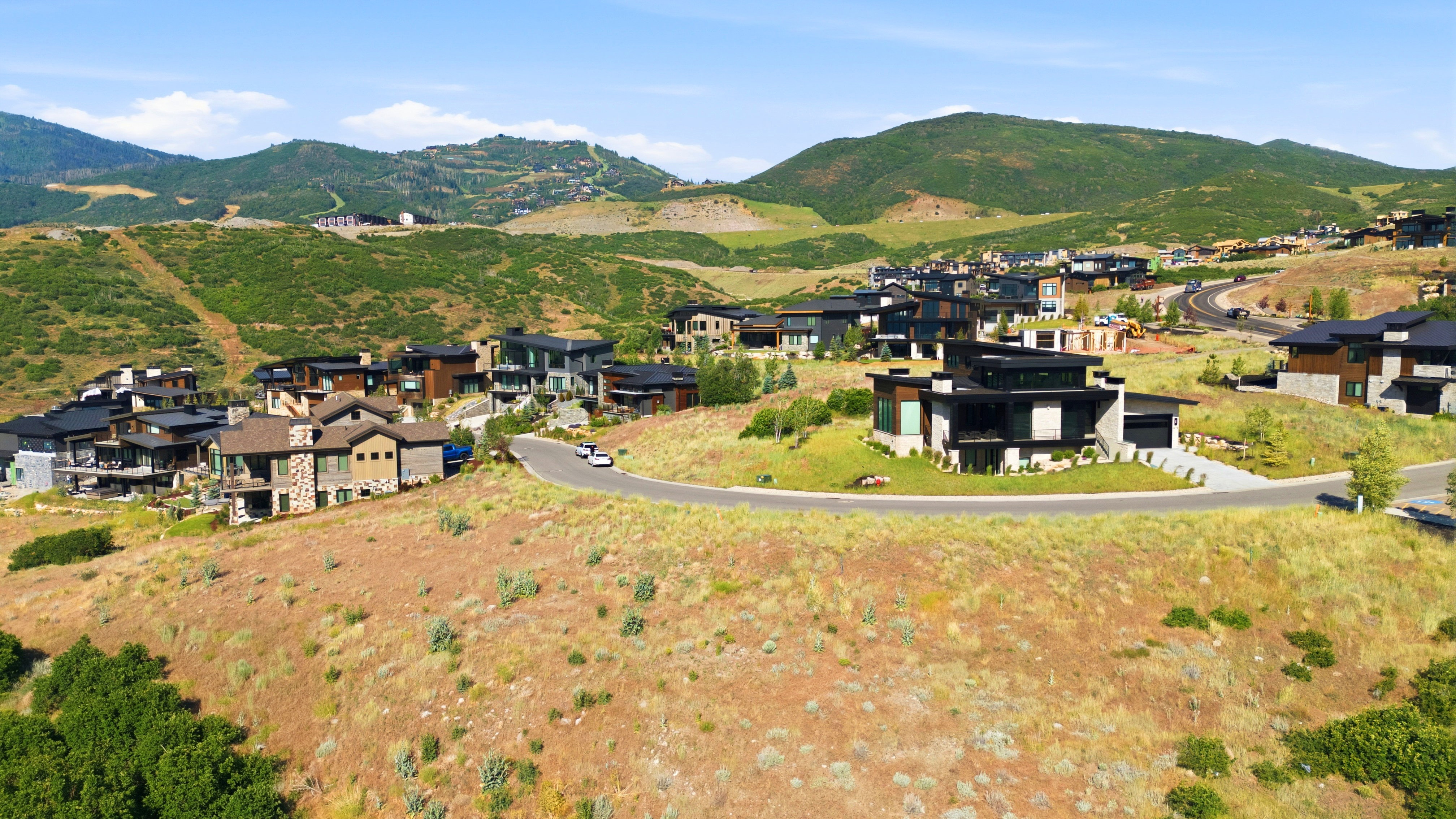 Hillside residential development featuring modern and traditional architectural styles, surrounded by natural terrain and distant mountains